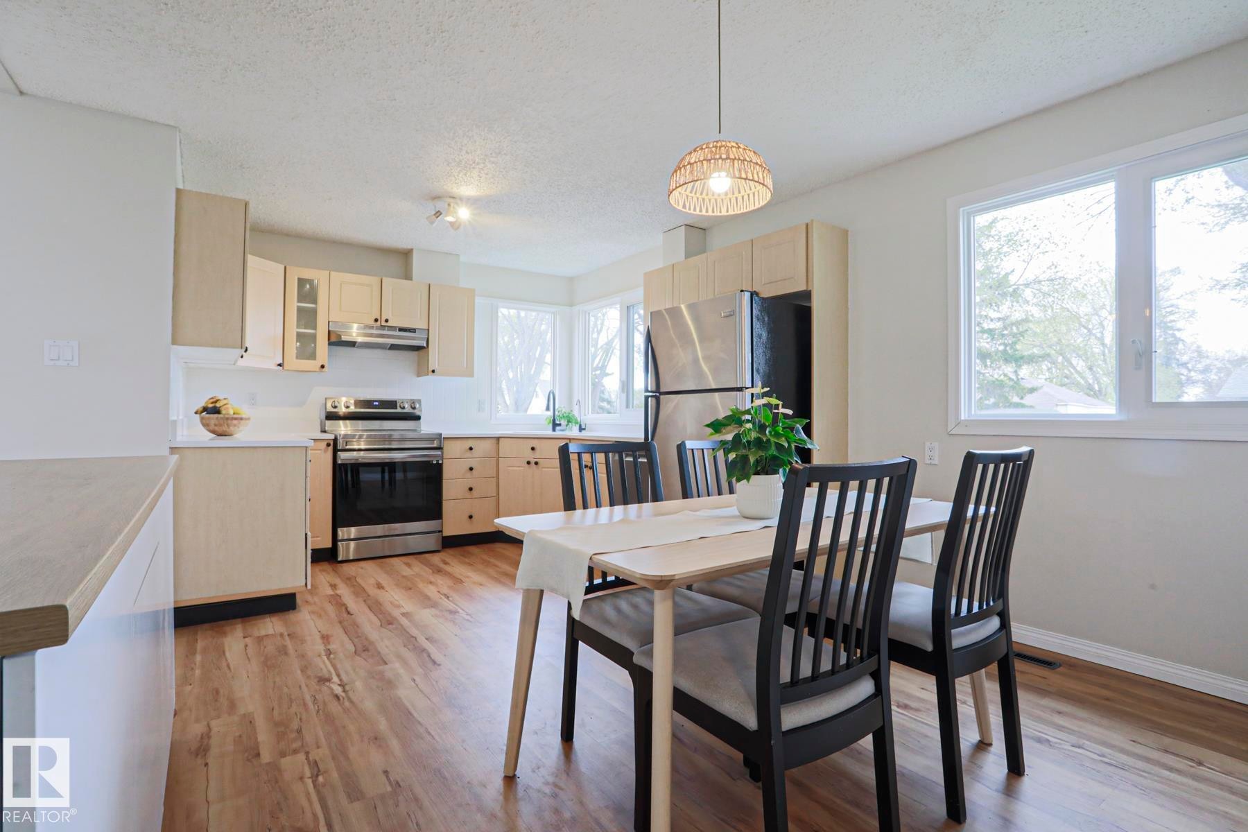 Open-concept kitchen and dining area featuring wood-finish flooring, light wood cabinetry, stainless steel appliances, and white countertops - 9523 151 Street, Edmonton, AB - Indoor