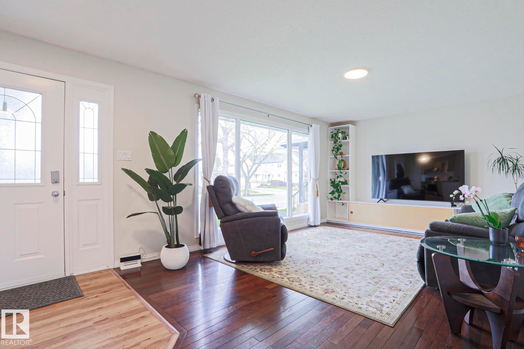 Inviting living space featuring rich wood-finish flooring, a large picture window, a white entry door with decorative glass inserts, and recessed ceiling lighting - 9523 151 Street, Edmonton, AB - Indoor Photo Showing Living Room