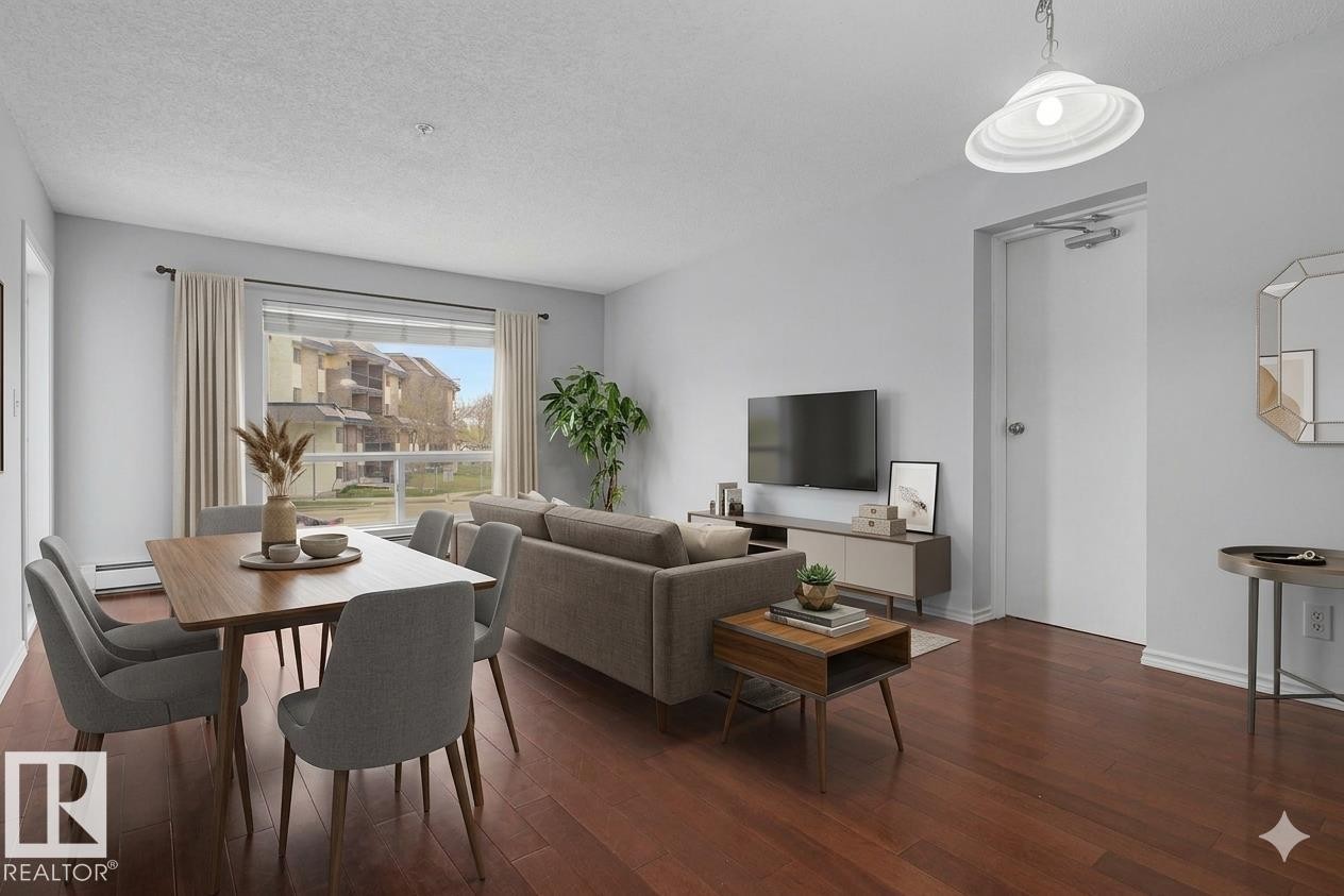Open-concept living space with dark wood-finish flooring, light-toned walls, and a large window - 213 17404 64 Avenue, Edmonton, AB