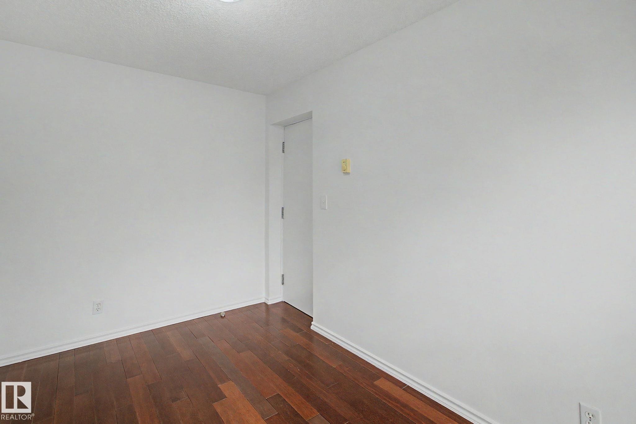 Wood-finish flooring with white baseboards, bright white walls, and a recessed ceiling light - 213 17404 64 Avenue, Edmonton, AB