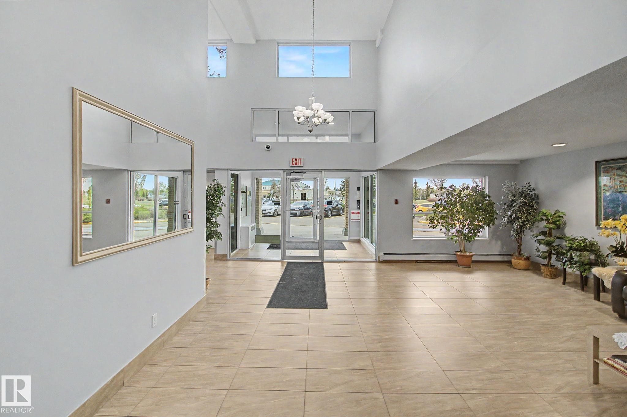 Bright common area featuring high ceilings, upper-level windows, and a multi-light chandelier - 213 17404 64 Avenue, Edmonton, AB