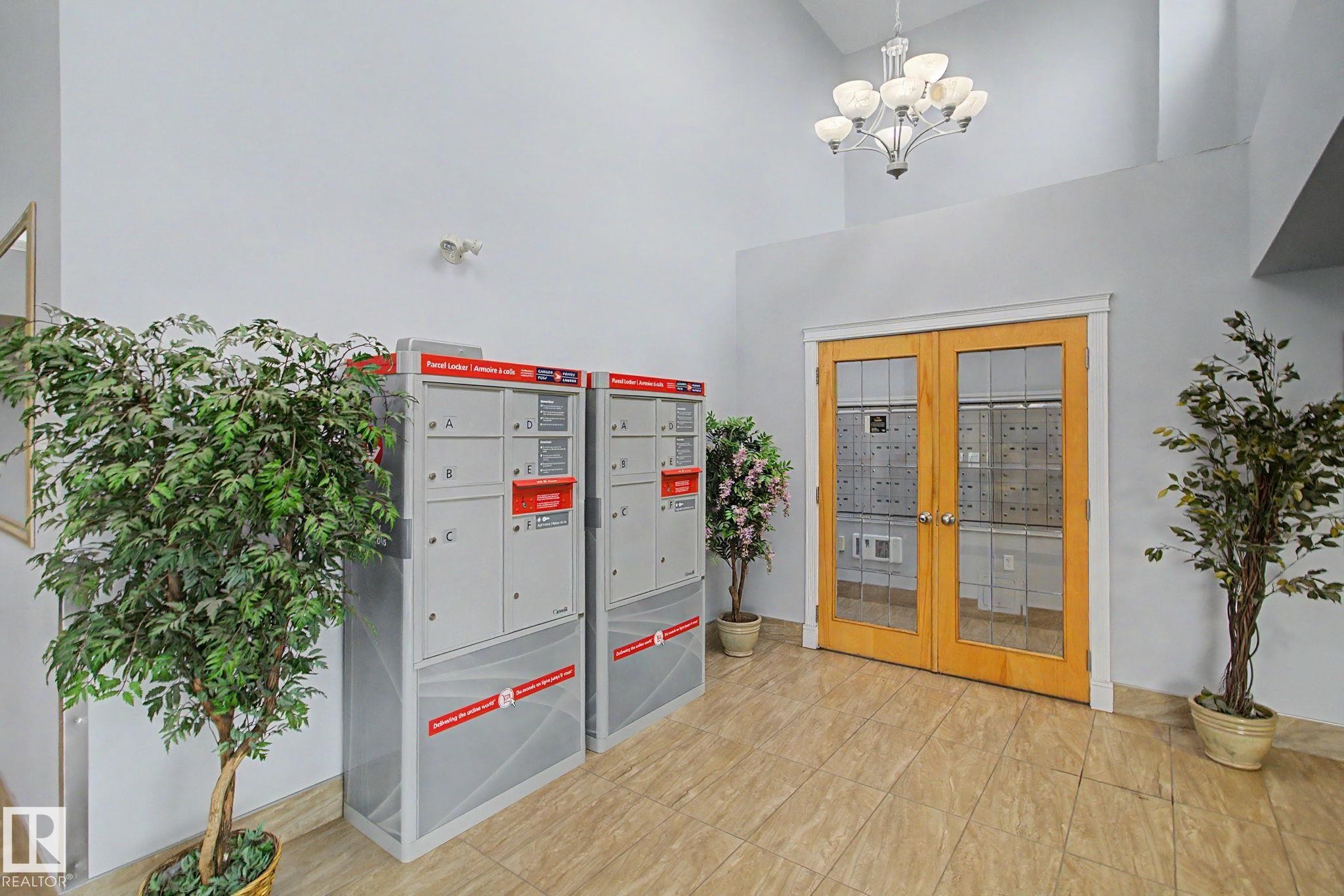 Building entryway featuring light-toned tile flooring and double glass-paneled doors with wood frames - 213 17404 64 Avenue, Edmonton, AB