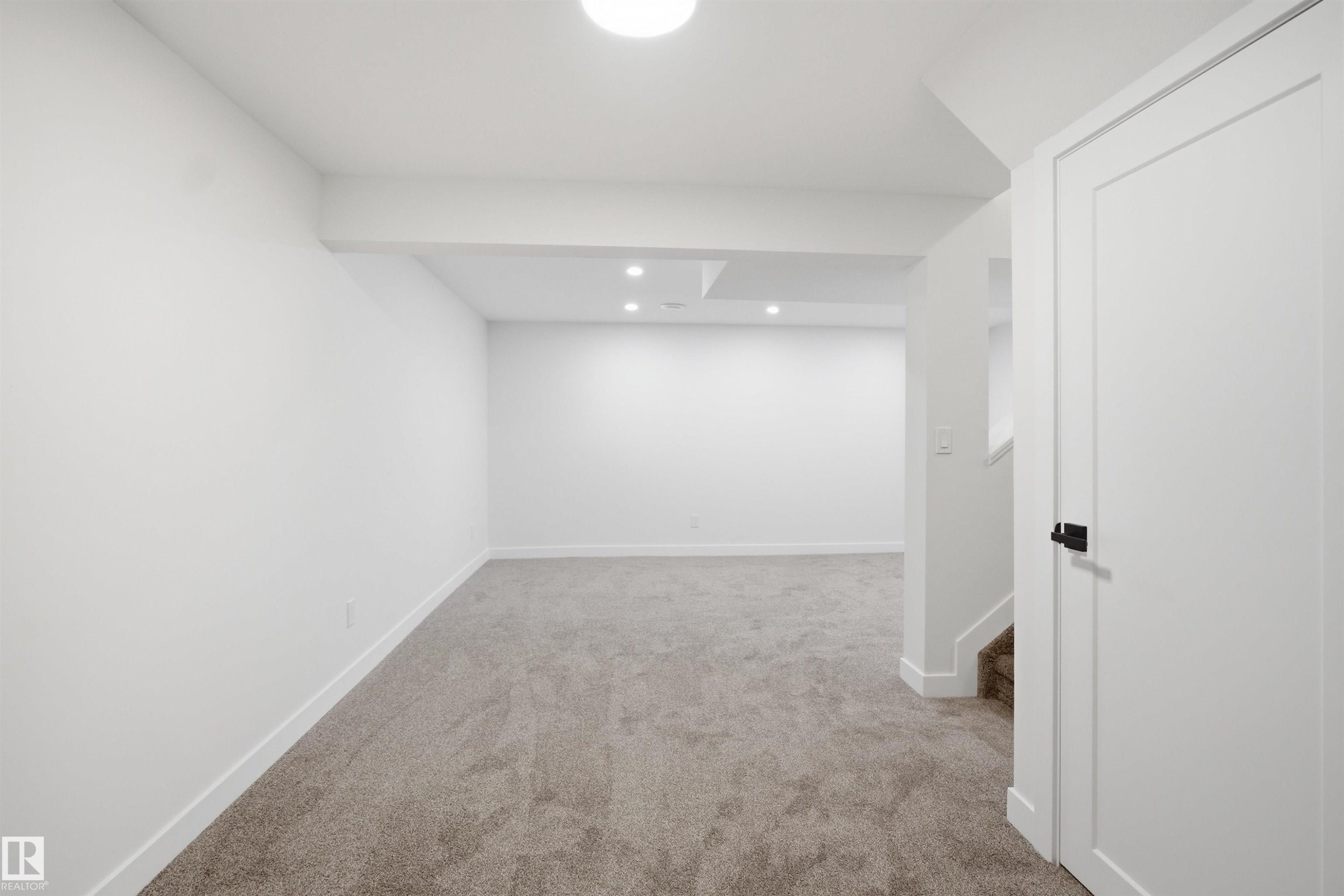 Expansive carpeted room featuring recessed lighting, a contemporary white door with matte black hardware, and crisp white baseboards - 1706 37 Street, Edmonton, AB - Indoor Photo Showing Other Room