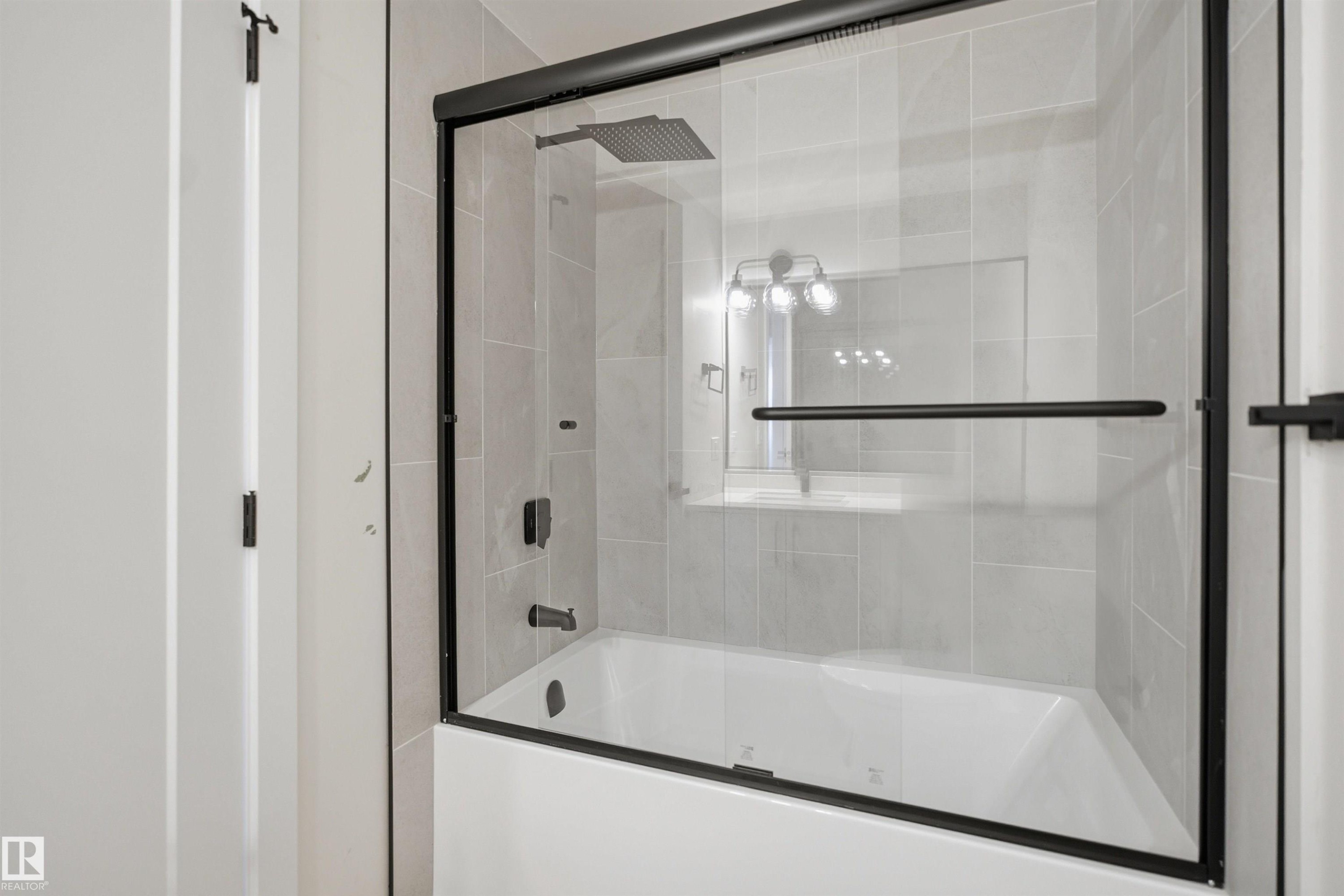 Shower-over-tub combination featuring a sliding glass enclosure with matte black framing and hardware - 1706 37 Street, Edmonton, AB - Indoor Photo Showing Bathroom