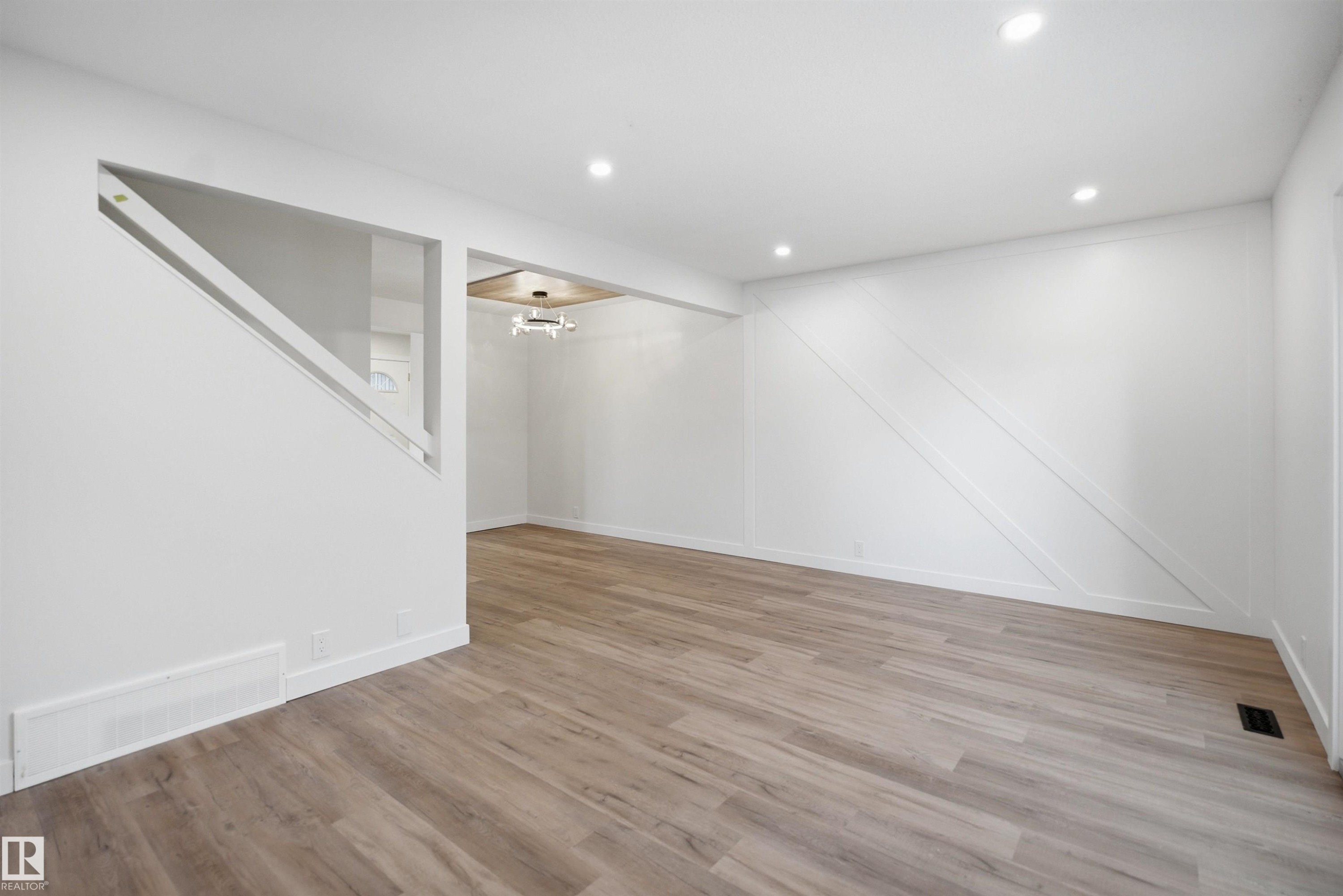 Spacious interior featuring wood-finish flooring, recessed lighting, and a decorative accent wall with diagonal paneling - 1706 37 Street, Edmonton, AB - Indoor Photo Showing Other Room