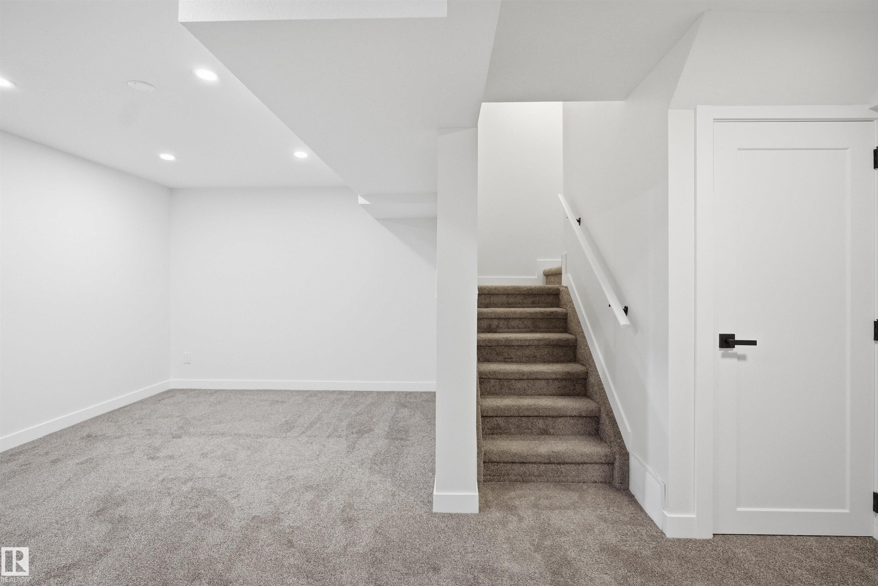 Carpeted recreation area featuring recessed lighting, a contemporary white door with black hardware, and a carpeted staircase with a white handrail - 1706 37 Street, Edmonton, AB - Indoor Photo Showing Other Room