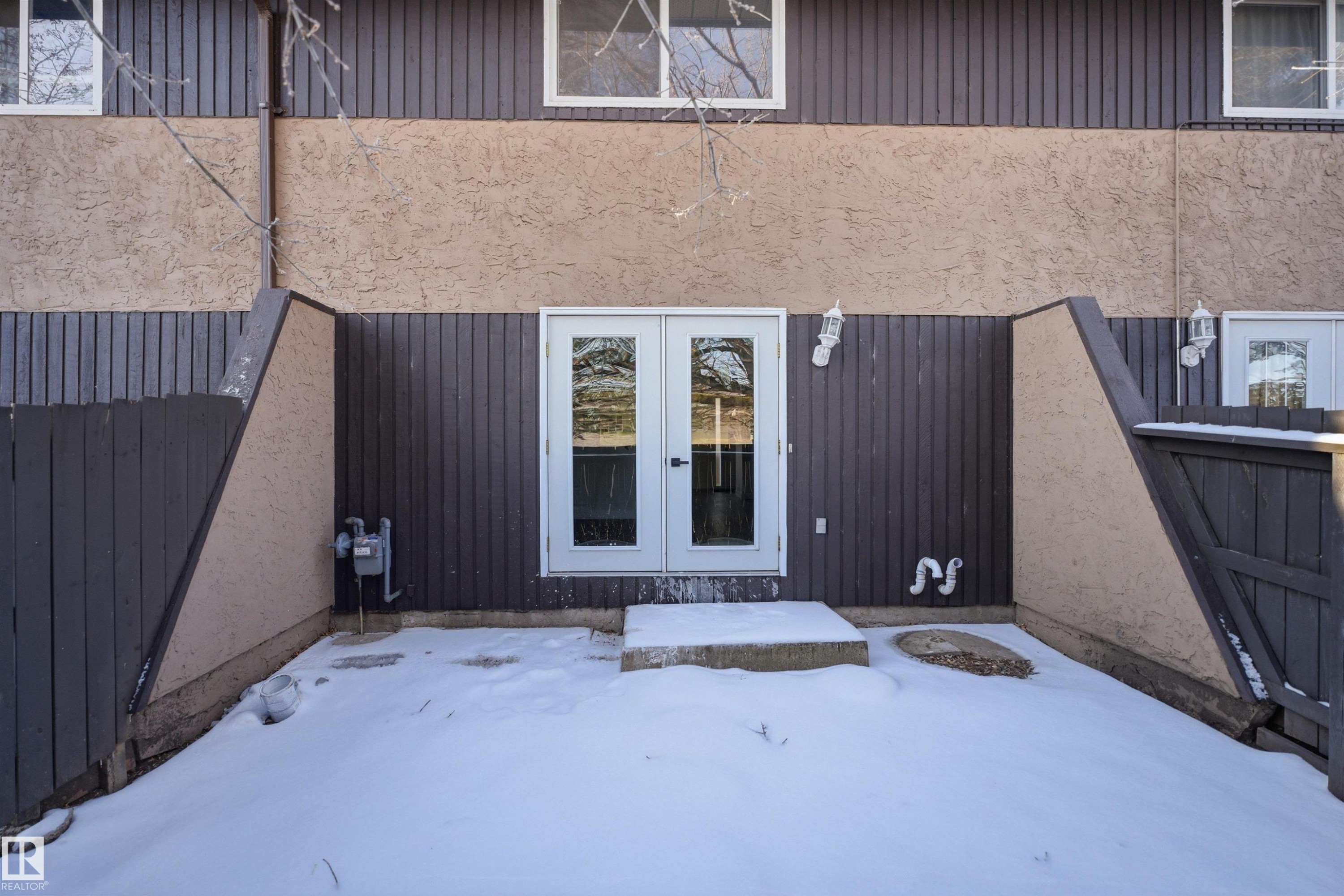 Rear exterior featuring double glass panel doors, stucco siding, vertical panel siding, and a privacy fence - 1706 37 Street, Edmonton, AB - Outdoor With Exterior