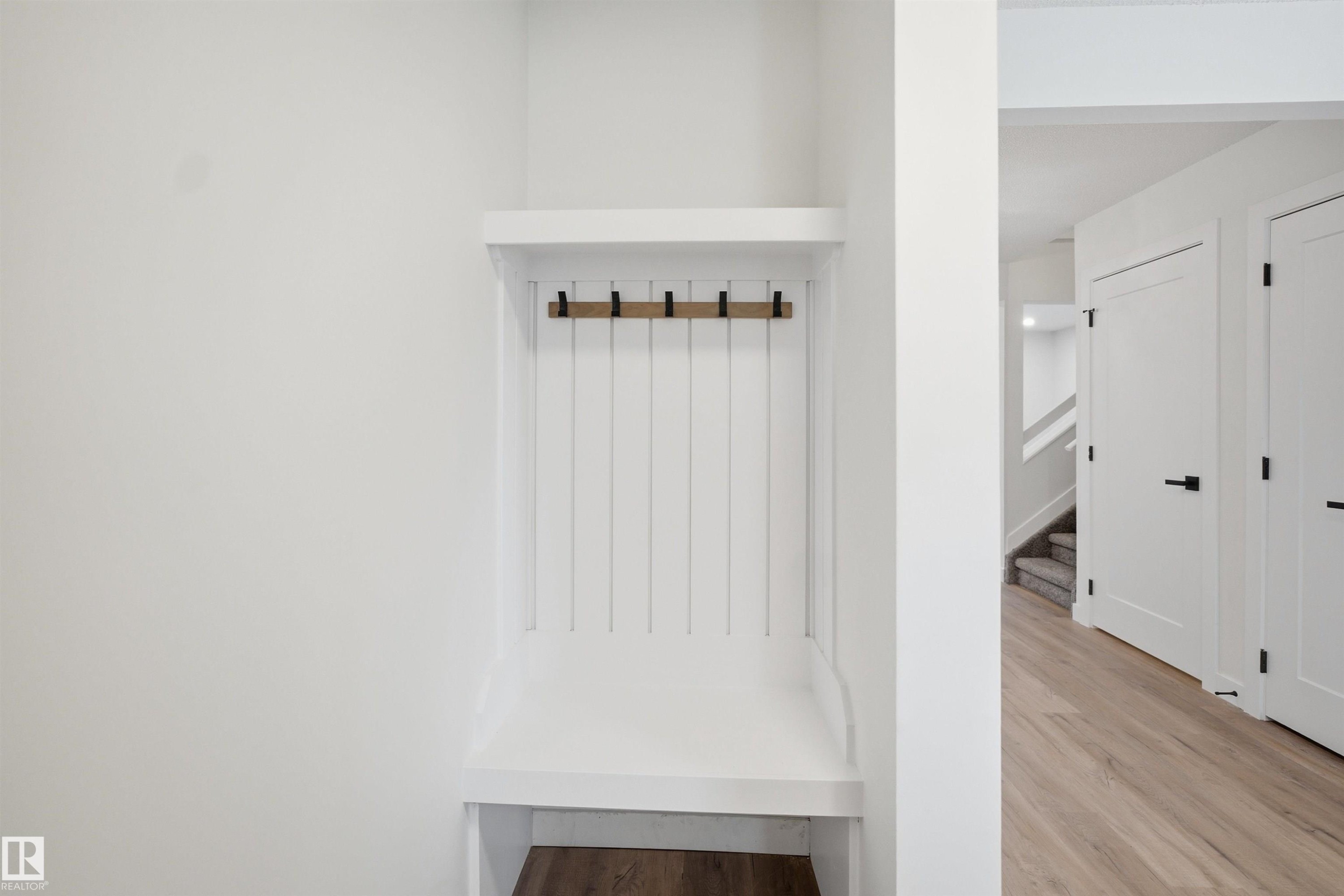 Built-in mudroom bench with coat hooks, crisp white shaker-style doors, and wood-finish flooring - 1706 37 Street, Edmonton, AB - Indoor Photo Showing Other Room