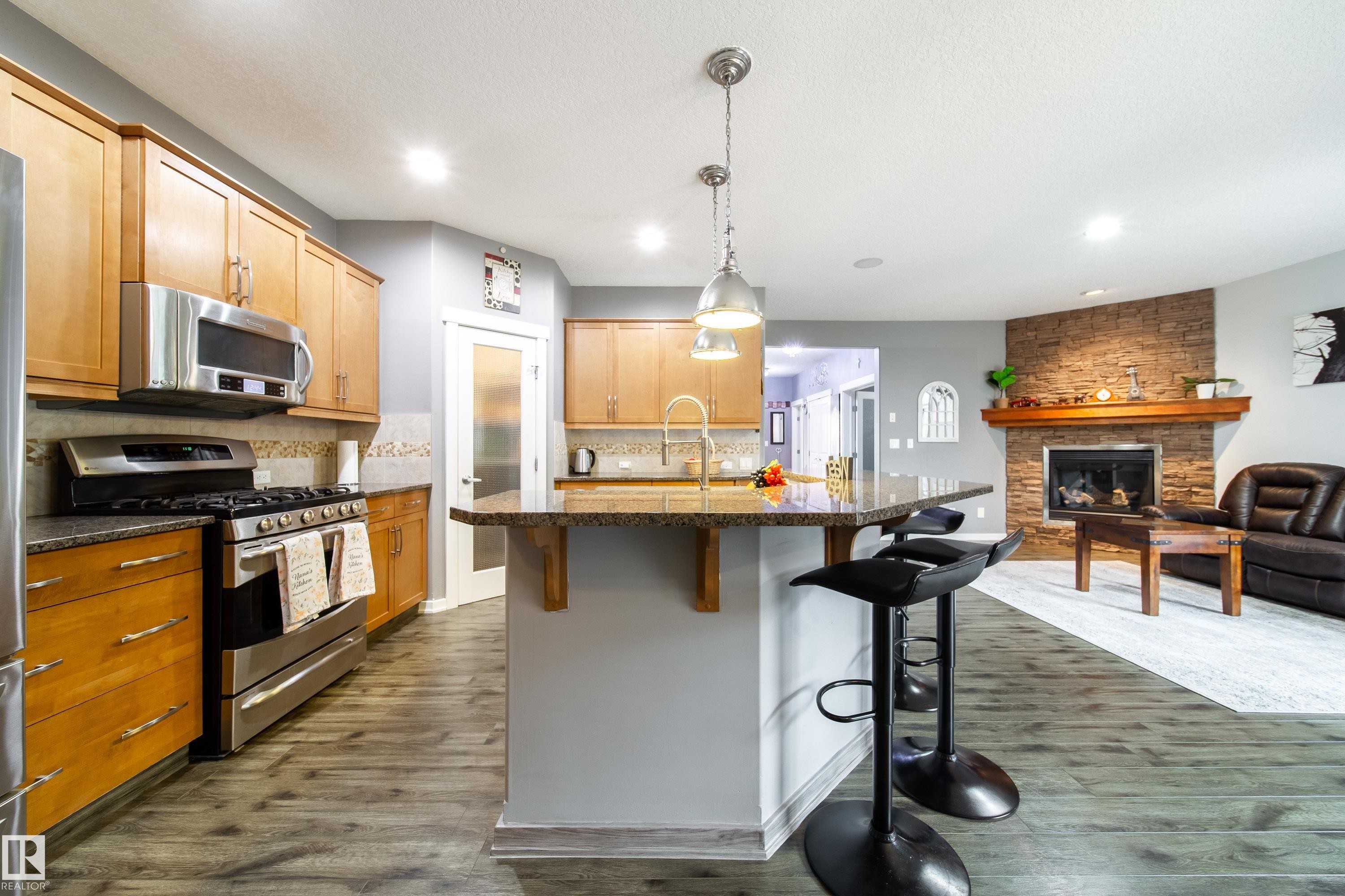 Kitchen featuring wood cabinetry, stainless steel appliances, speckled stone countertops, and a peninsula with pendant lighting - 2016 125 Street, Edmonton, AB - Indoor Photo Showing Kitchen With Fireplace With Upgraded Kitchen
