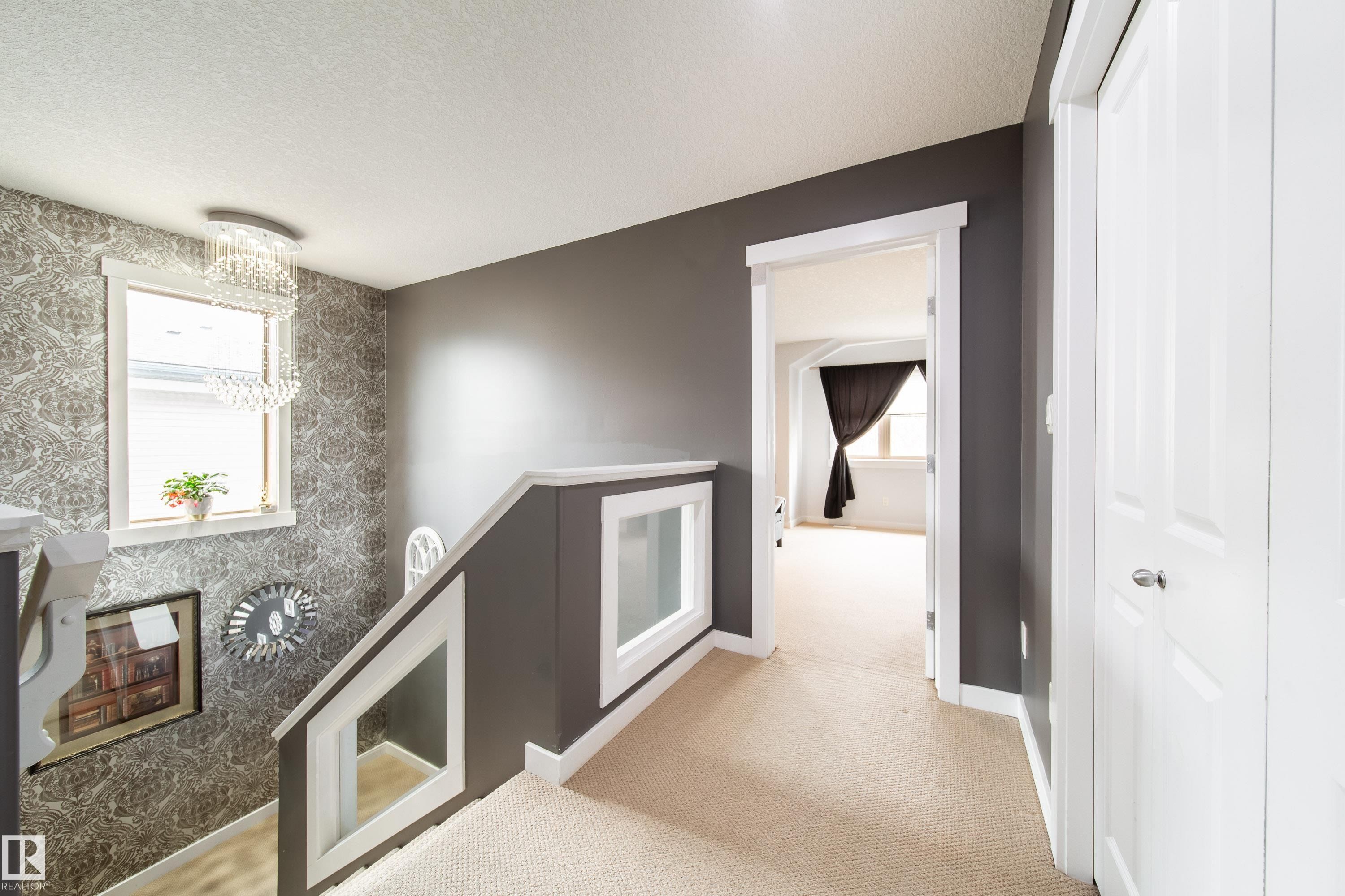 Upper-level landing featuring a crystal chandelier, patterned accent wall, and a carpeted floor - 2016 125 Street, Edmonton, AB - Indoor Photo Showing Other Room