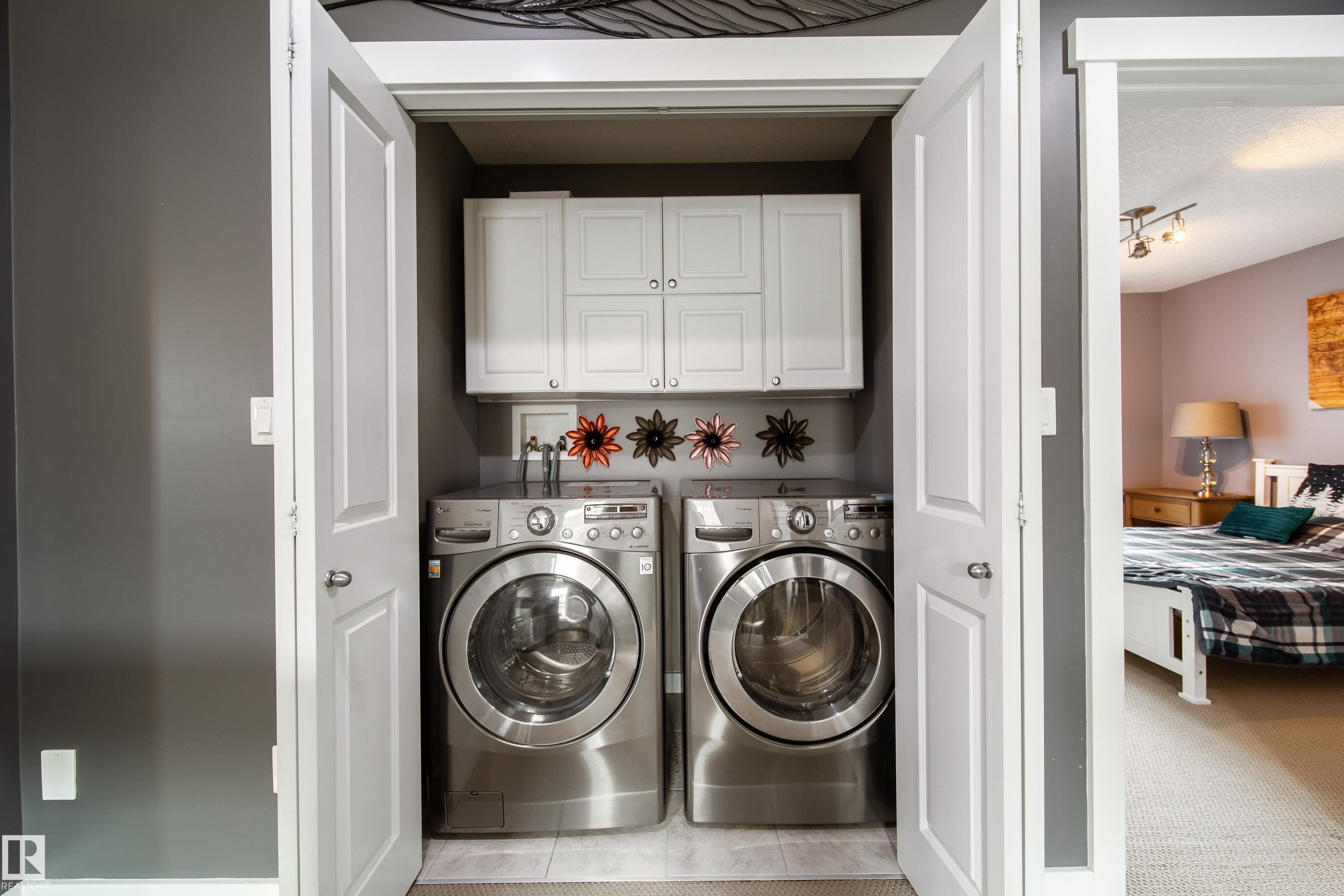 Dedicated laundry closet featuring a stacked washer and dryer, upper cabinetry, and a tile floor - 2016 125 Street, Edmonton, AB - Indoor Photo Showing Laundry Room