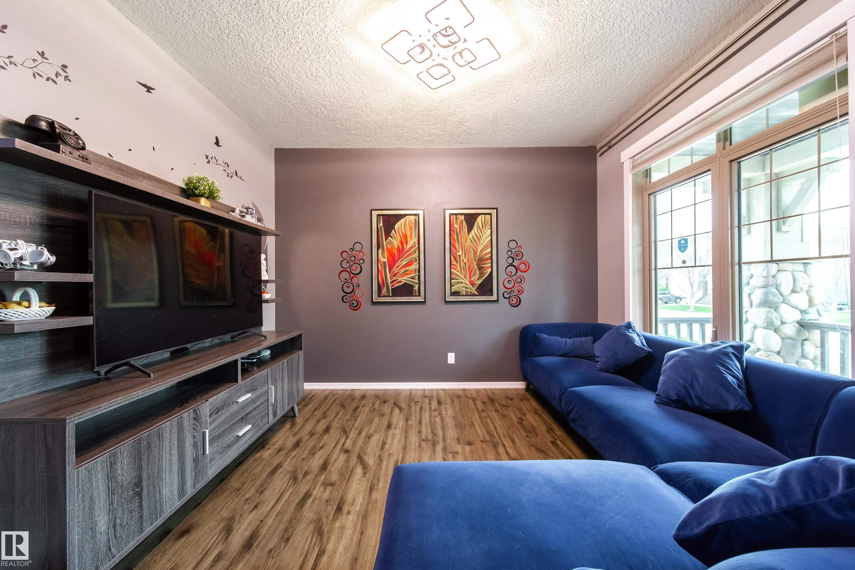 Living area featuring wood-finish flooring, a contemporary ceiling light fixture, a built-in media console with open shelving and drawers, large multi-pane windows, and a neutral wall color palette - 2016 125 Street, Edmonton, AB - Indoor
