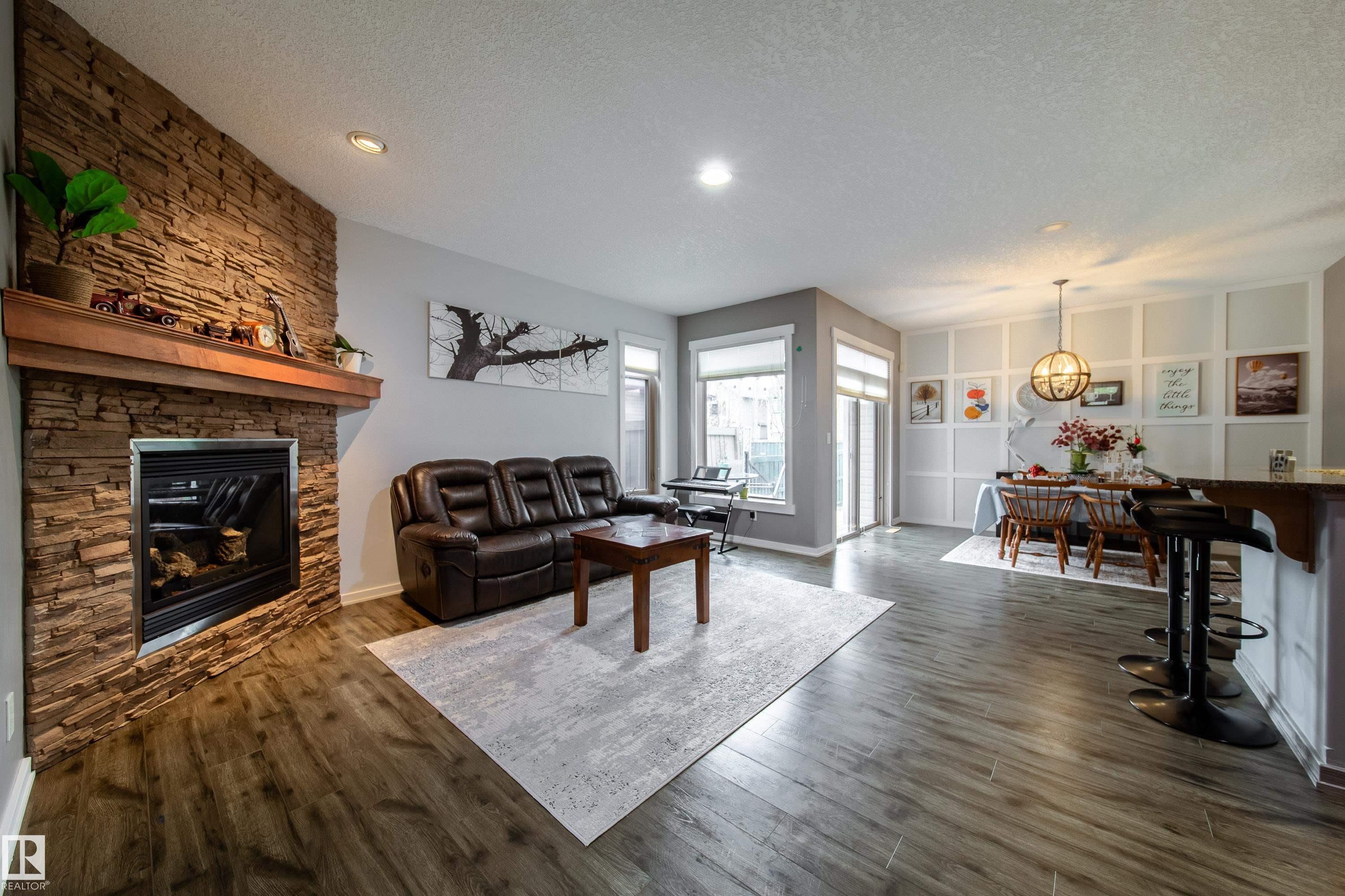 Spacious living area featuring a stone-clad fireplace with a wood mantel, wood-finish flooring, recessed lighting, and large windows with blinds - 2016 125 Street, Edmonton, AB - Indoor Photo Showing Living Room With Fireplace