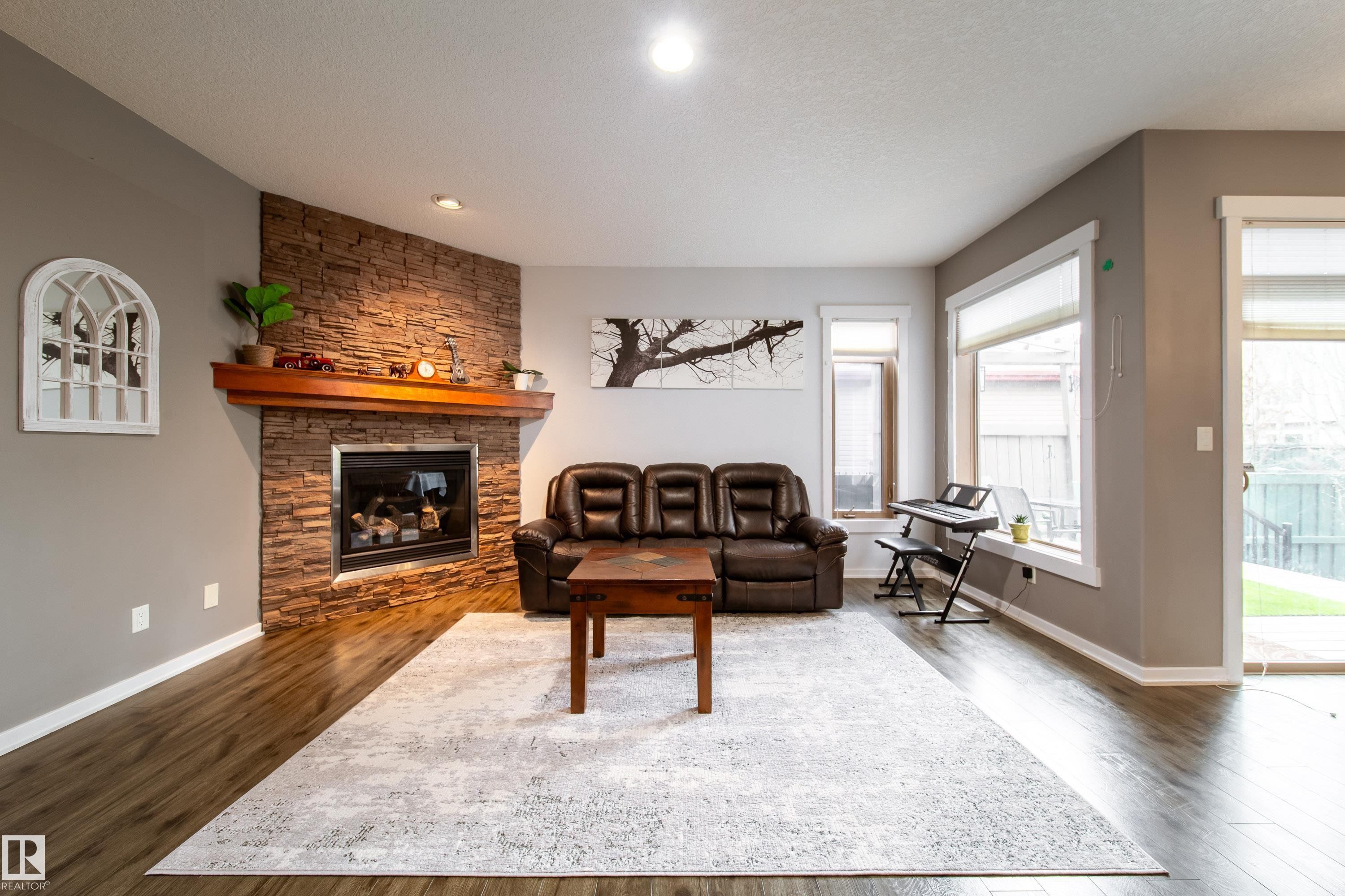 Living area featuring a stone-faced fireplace with a wood mantel, wood-finish flooring, recessed lighting, and multiple windows - 2016 125 Street, Edmonton, AB - Indoor Photo Showing Living Room With Fireplace
