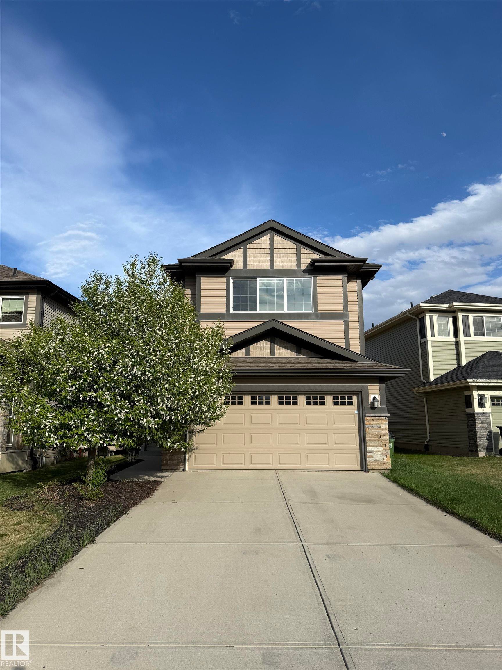Two-story residence featuring tan siding with dark trim accents, an attached two-car garage, and a concrete driveway - 4723 Alwood Bend Sw, Edmonton, AB - Outdoor