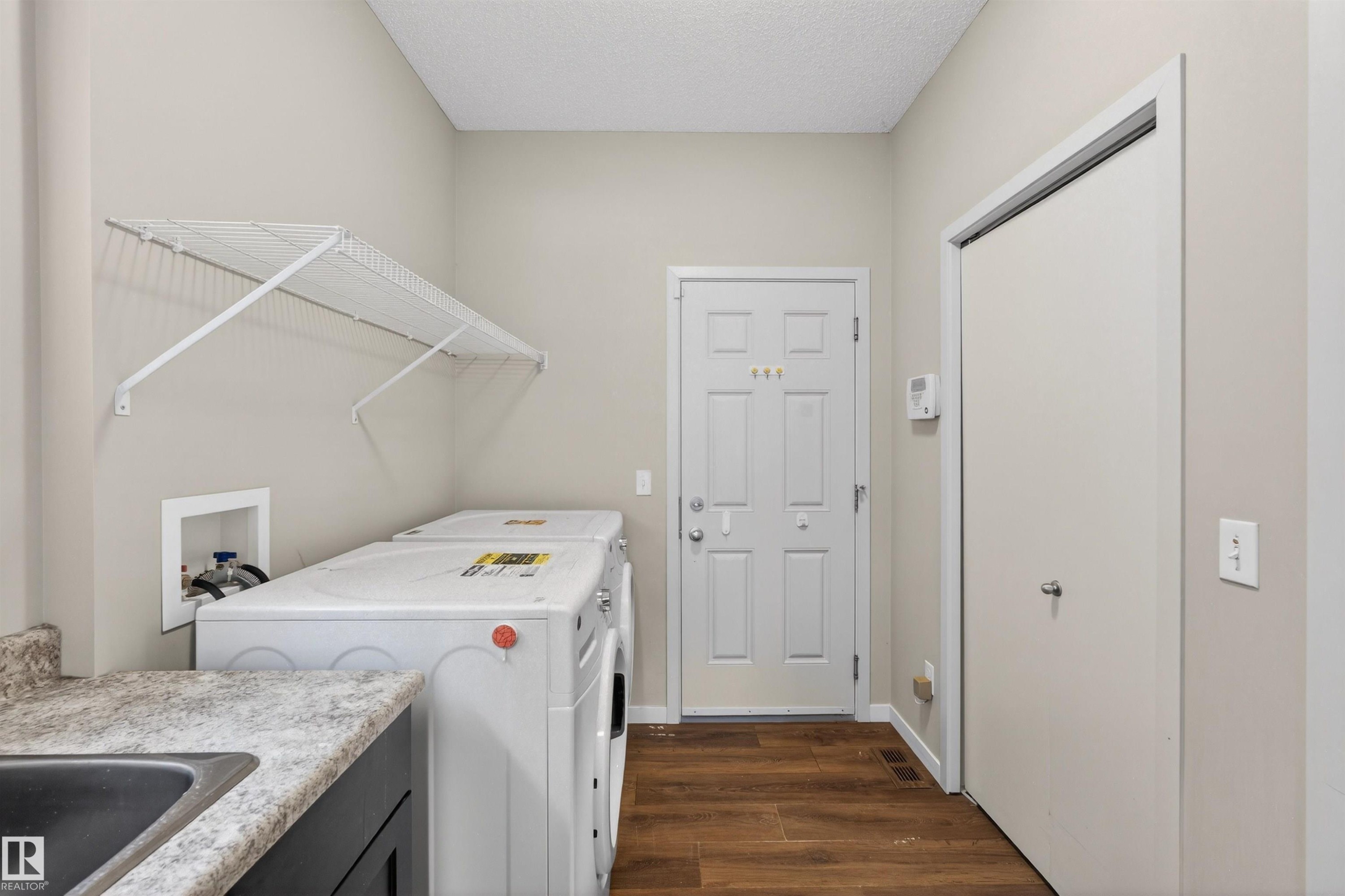 Laundry area featuring wood-finish flooring, a utility sink with a laminate countertop, and overhead wire shelving - 4723 Alwood Bend Sw, Edmonton, AB - Indoor Photo Showing Laundry Room