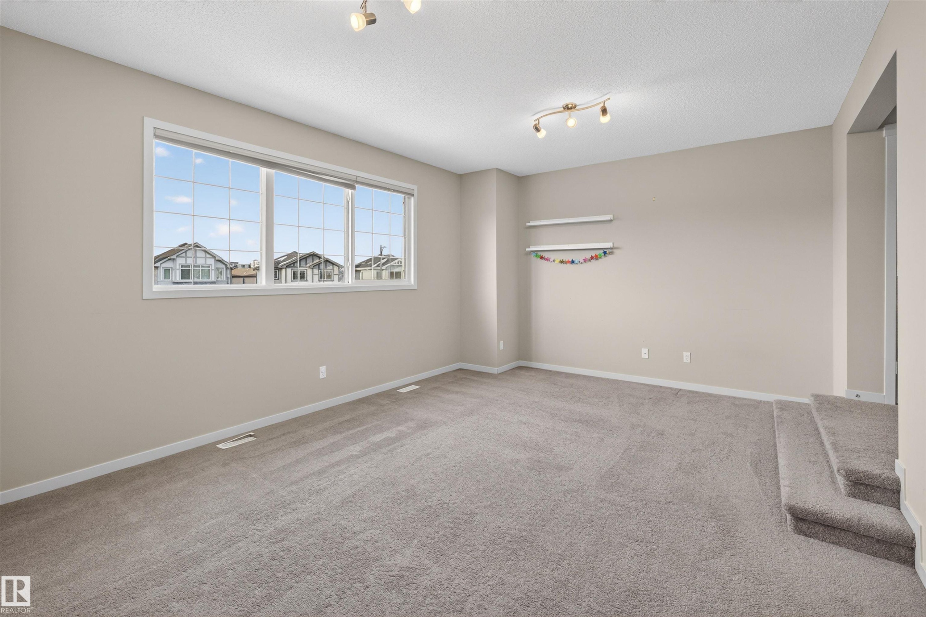 Neutral-toned room featuring a large multi-pane window, track lighting, and carpeted flooring - 4723 Alwood Bend Sw, Edmonton, AB - Indoor Photo Showing Other Room