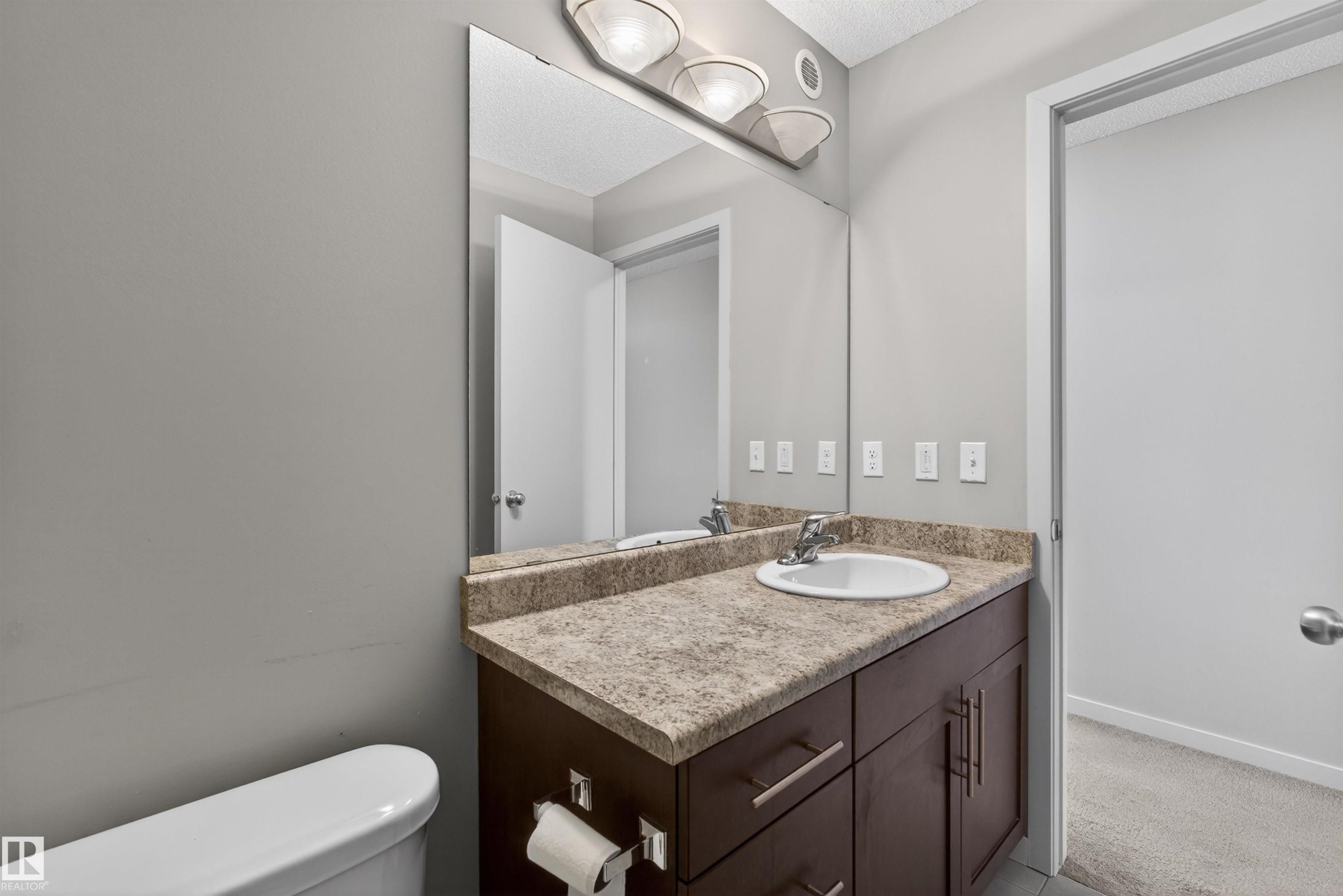 Bathroom vanity featuring a dark wood-finish cabinet with silver hardware, an integrated white sink, and a speckled countertop - 4723 Alwood Bend Sw, Edmonton, AB - Indoor Photo Showing Bathroom