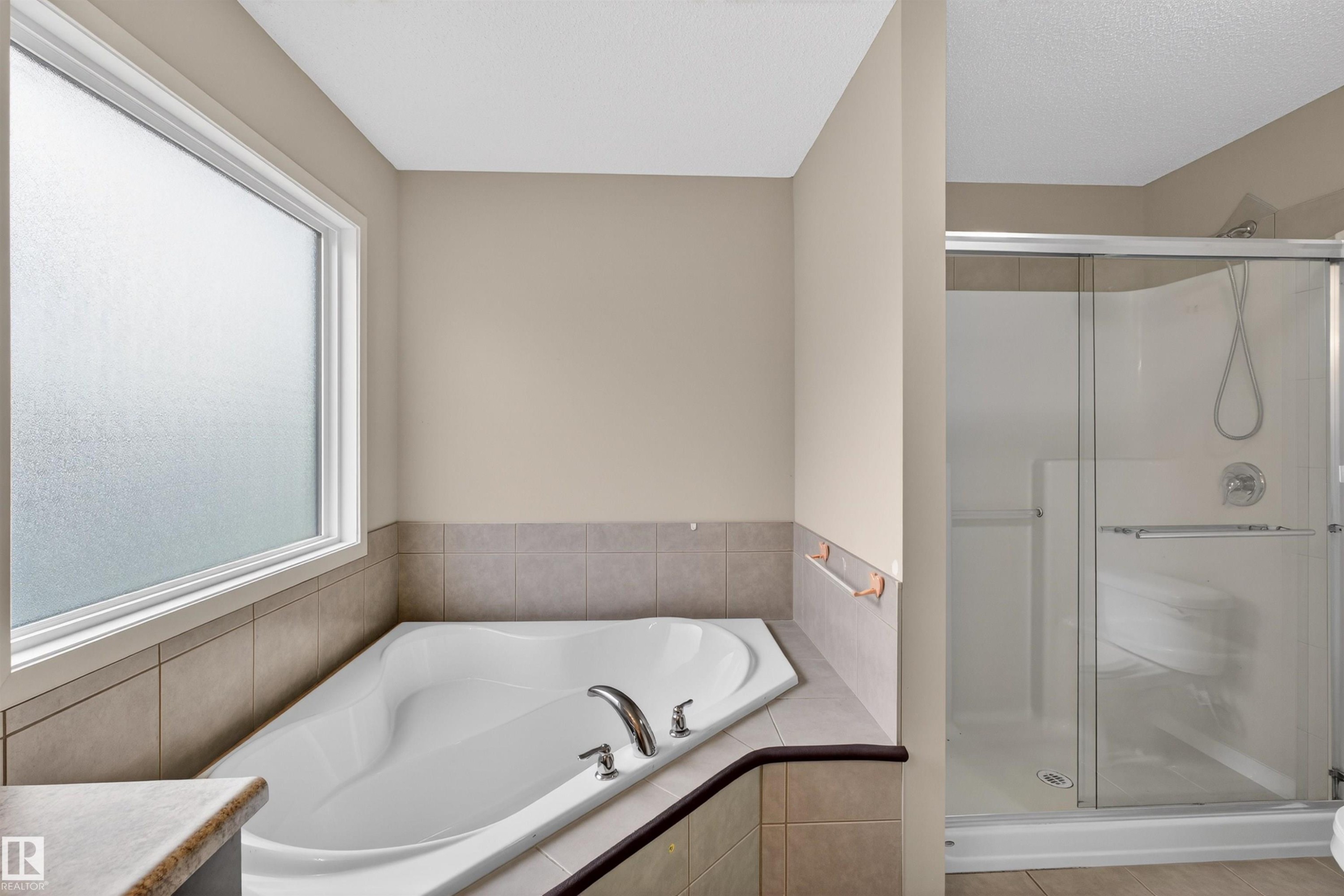 Soaking tub with chrome fixtures, tiled surround, and frosted window - 4723 Alwood Bend Sw, Edmonton, AB - Indoor Photo Showing Bathroom