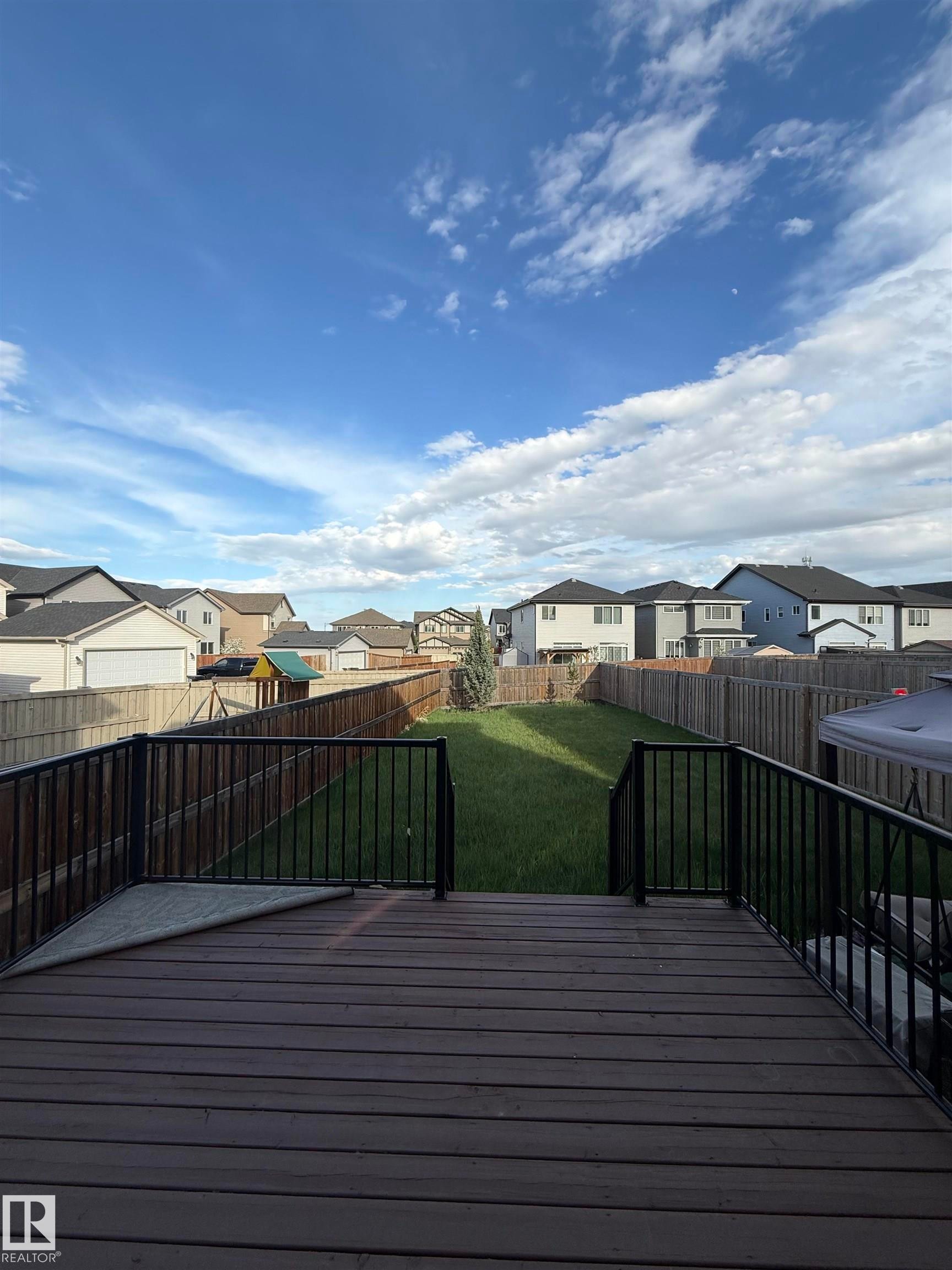Spacious backyard featuring a large composite deck with black metal railings, a manicured lawn, and perimeter wood fencing - 4723 Alwood Bend Sw, Edmonton, AB - Outdoor