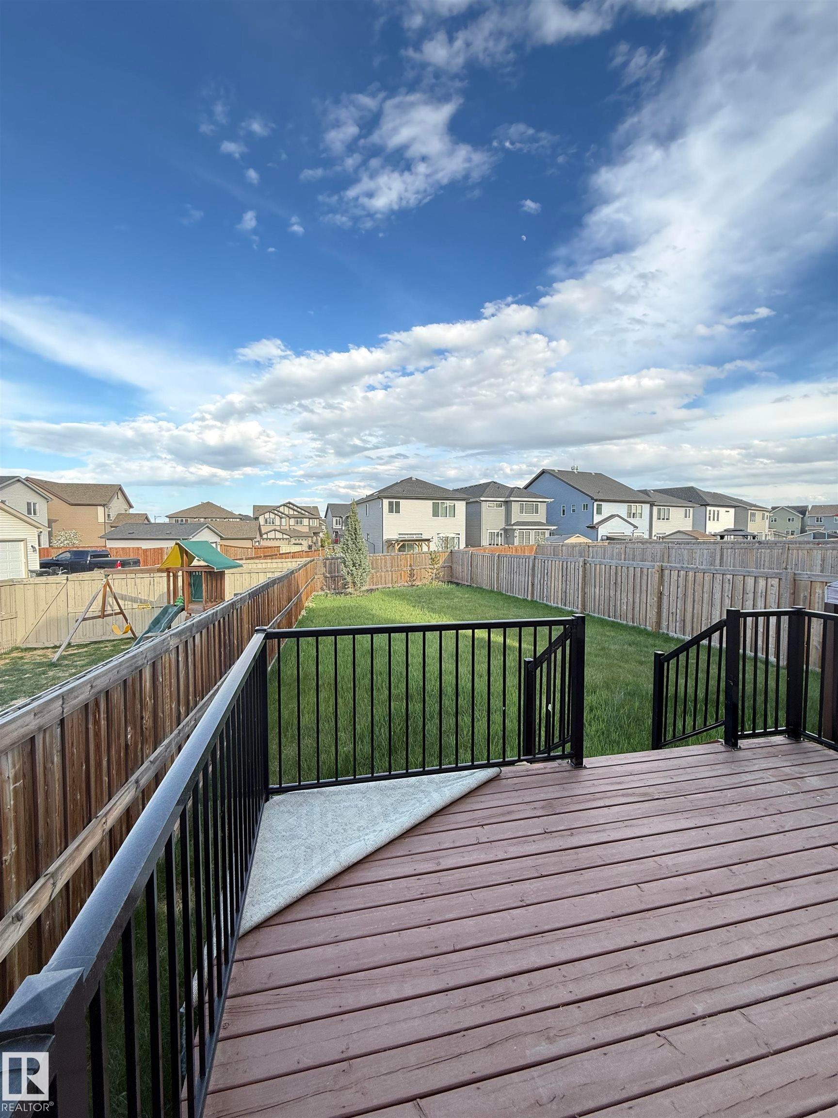Spacious outdoor deck with dark wood-finish planks and black metal railings, overlooking a large grassy yard enclosed by wood fencing - 4723 Alwood Bend Sw, Edmonton, AB - Outdoor