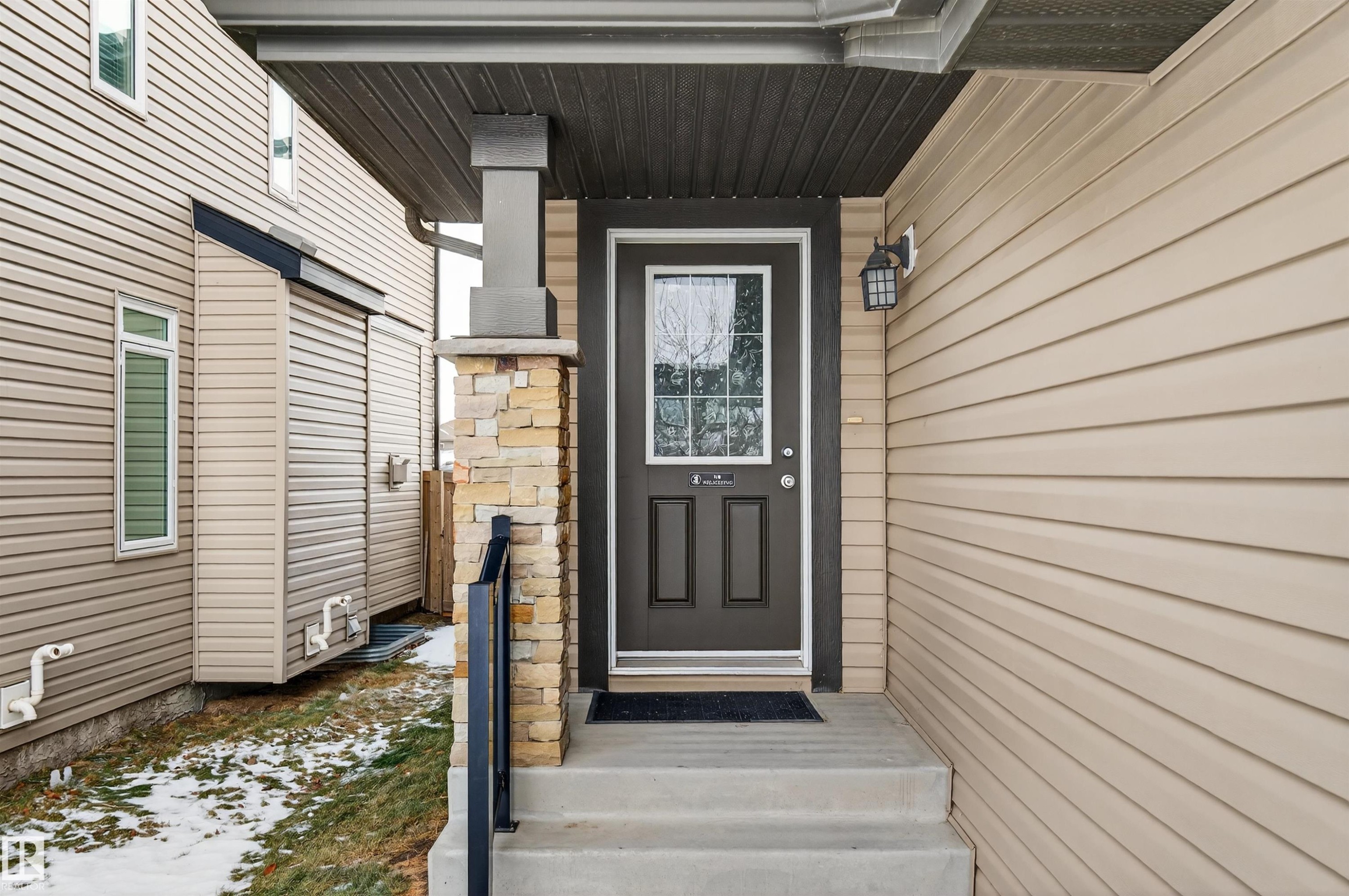 Entryway featuring a dark paneled front door with decorative window inserts, an exterior wall light fixture, and concrete steps - 4723 Alwood Bend Sw, Edmonton, AB - Outdoor With Exterior