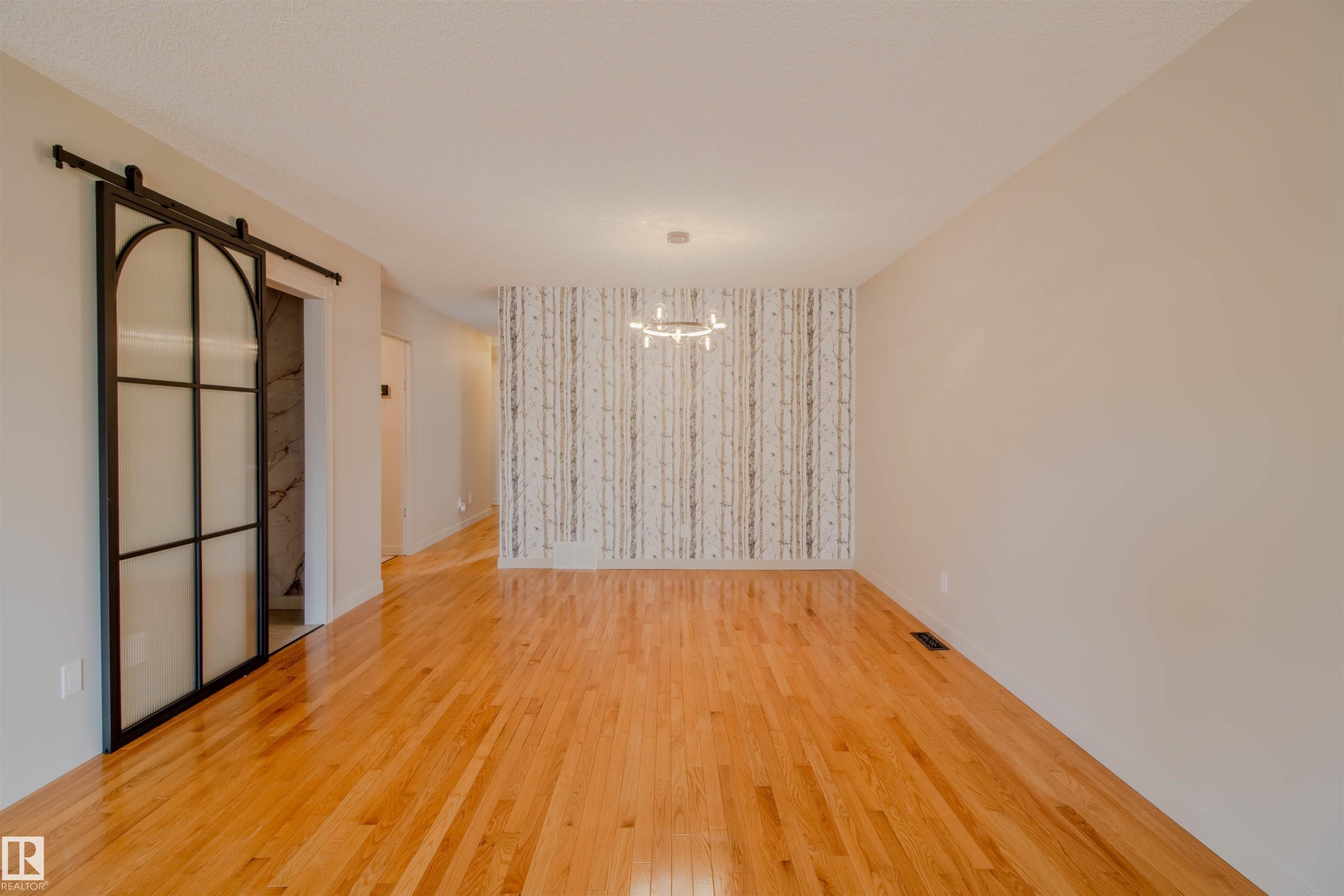 Open-concept room featuring wood flooring, a decorative accent wall, and a contemporary chandelier - 5935 189 Street, Edmonton, AB - Indoor Photo Showing Other Room