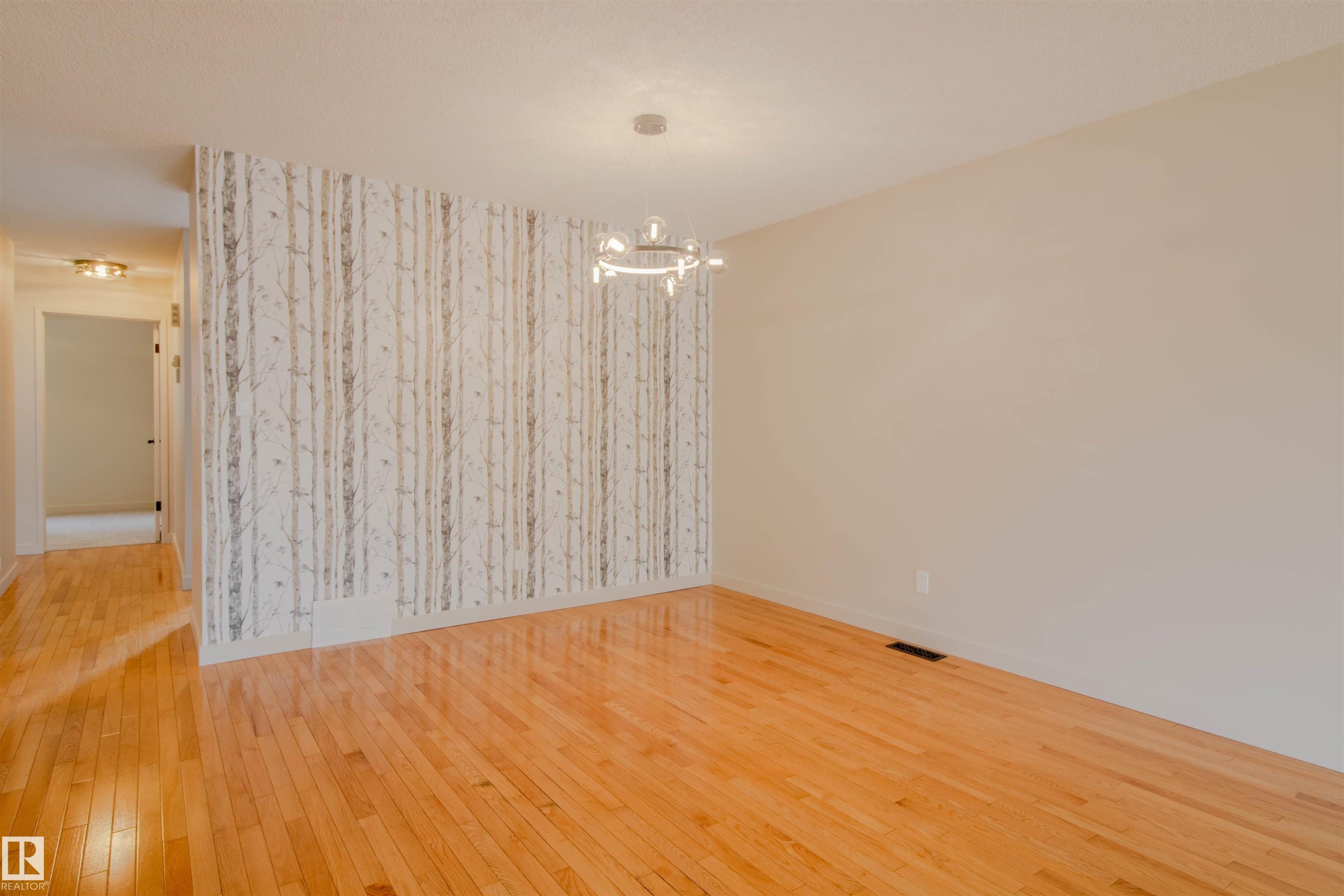 Hardwood flooring extends throughout this space, featuring a distinct accent wall with a tree-patterned design - 5935 189 Street, Edmonton, AB - Indoor Photo Showing Other Room