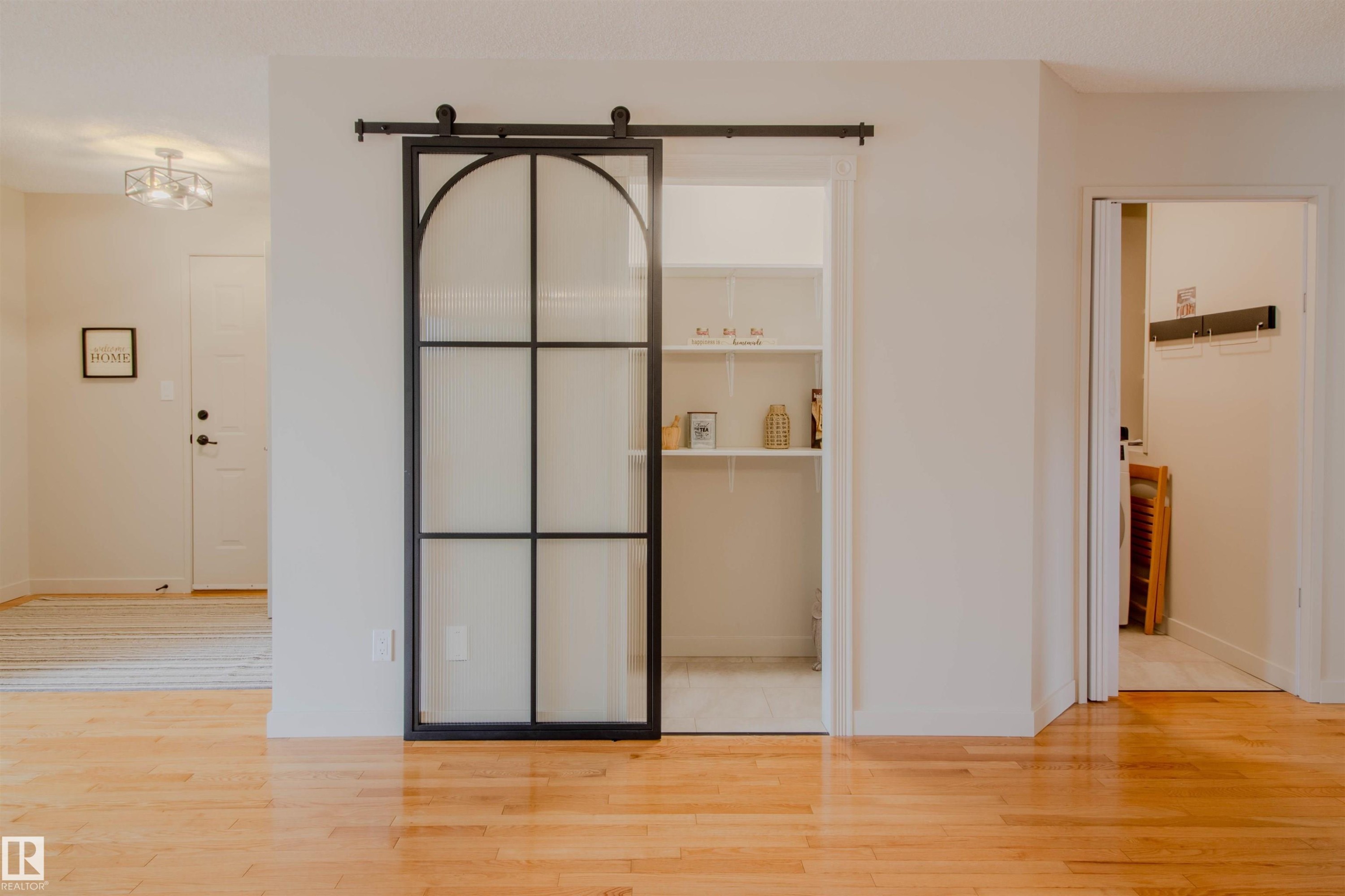 Hardwood-finish flooring extending through an interior space featuring a black-framed barn door with frosted glass panels - 5935 189 Street, Edmonton, AB - Indoor Photo Showing Other Room
