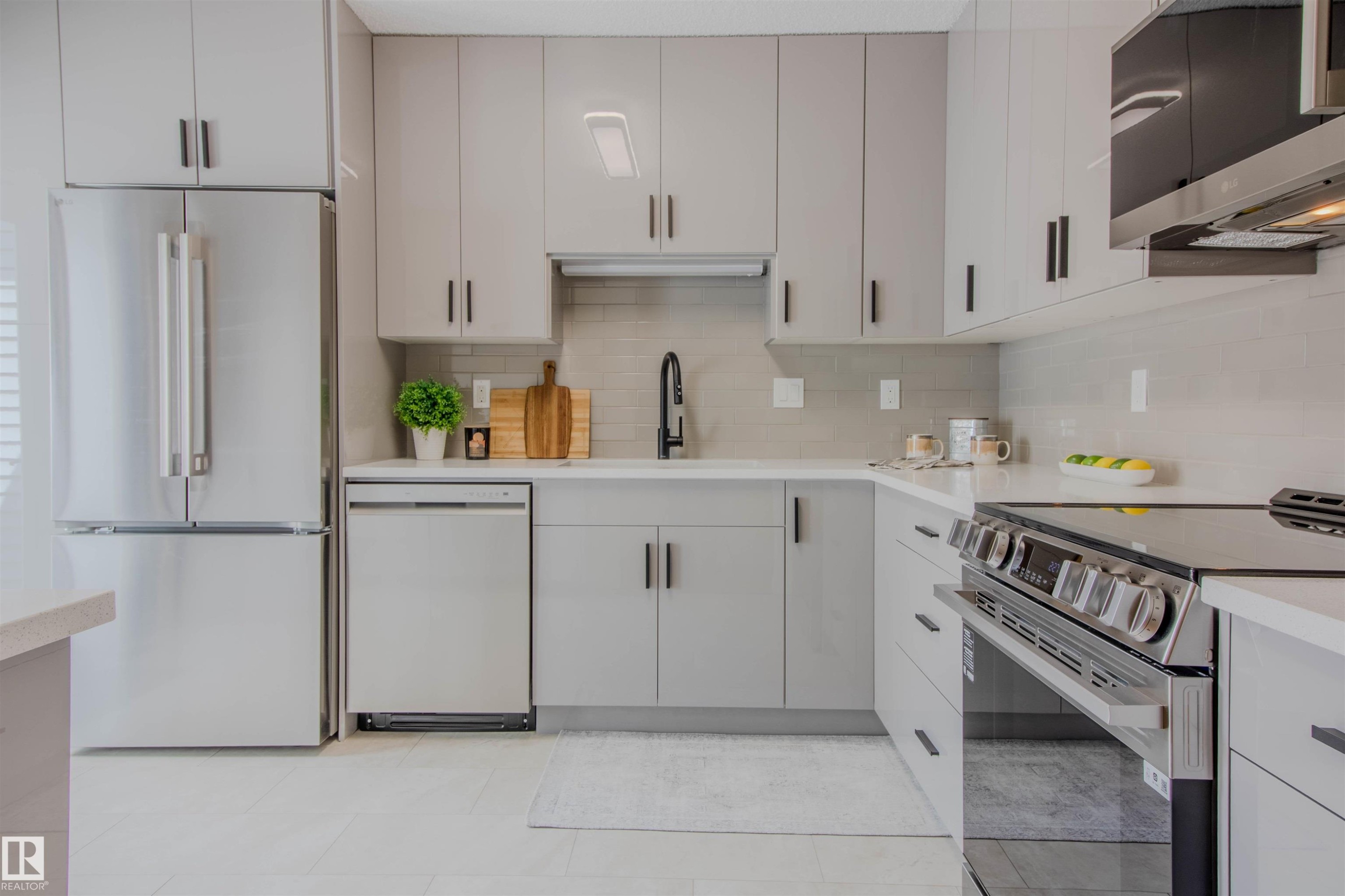 Contemporary kitchen featuring light gray cabinetry with black hardware, stainless steel appliances, white countertops, a gray tiled backsplash, and recessed lighting - 5935 189 Street, Edmonton, AB - Indoor Photo Showing Kitchen With Upgraded Kitchen