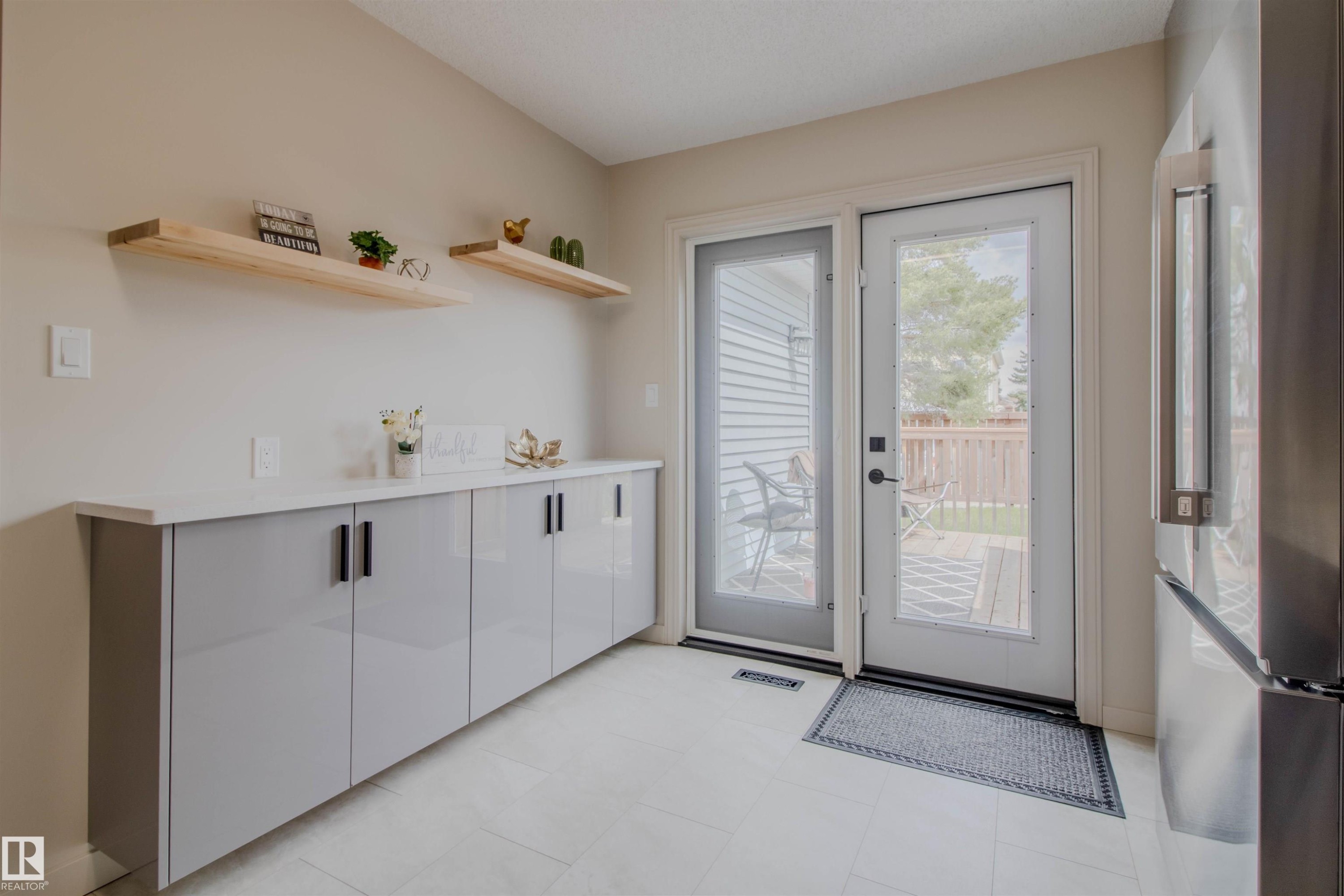 Contemporary cabinetry with a light countertop and wood floating shelves, complemented by light tile flooring - 5935 189 Street, Edmonton, AB - Indoor Photo Showing Other Room