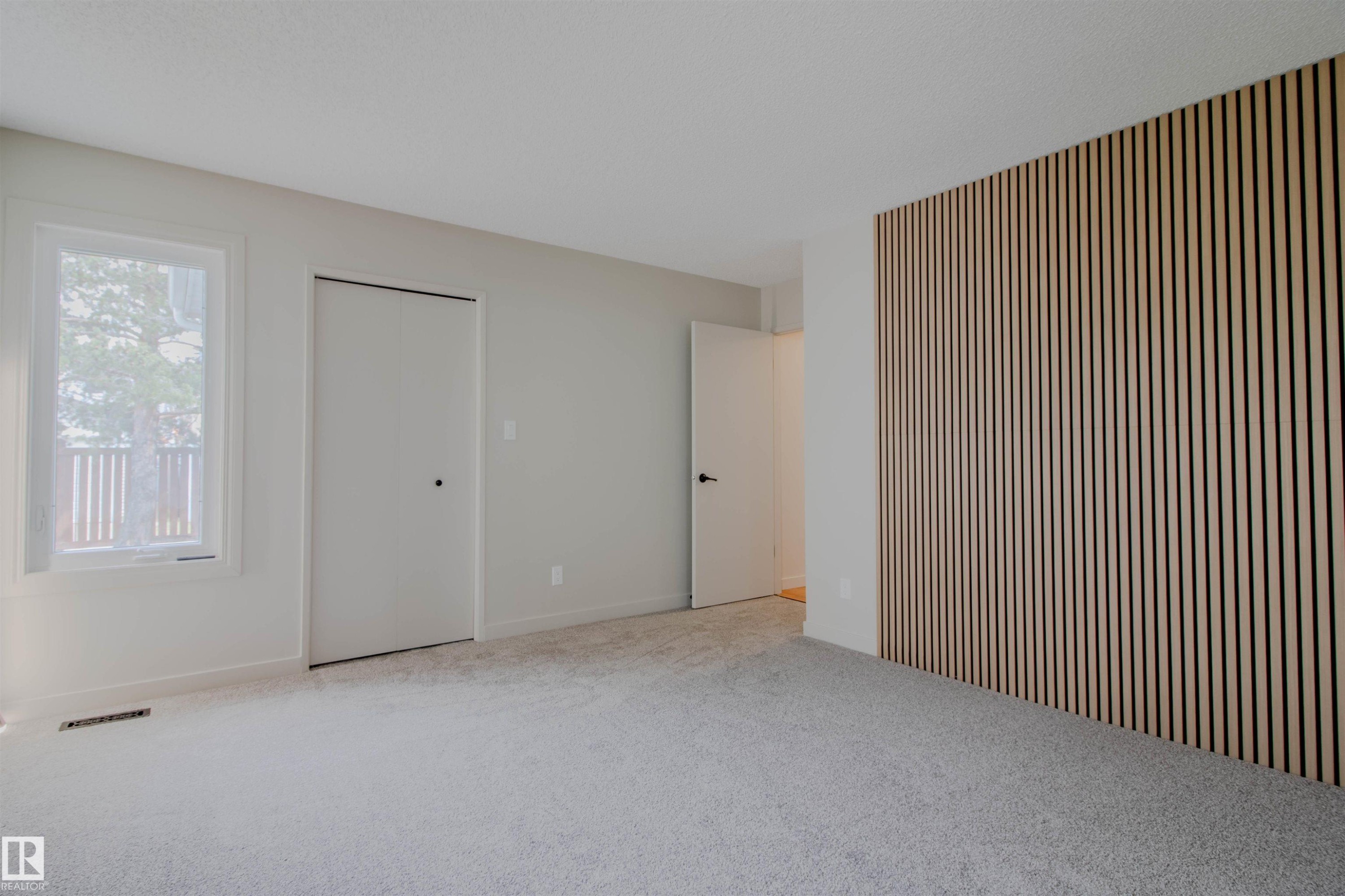 Interior space featuring a slatted wood accent wall, light gray carpeting, and a white framed window - 5935 189 Street, Edmonton, AB - Indoor Photo Showing Other Room