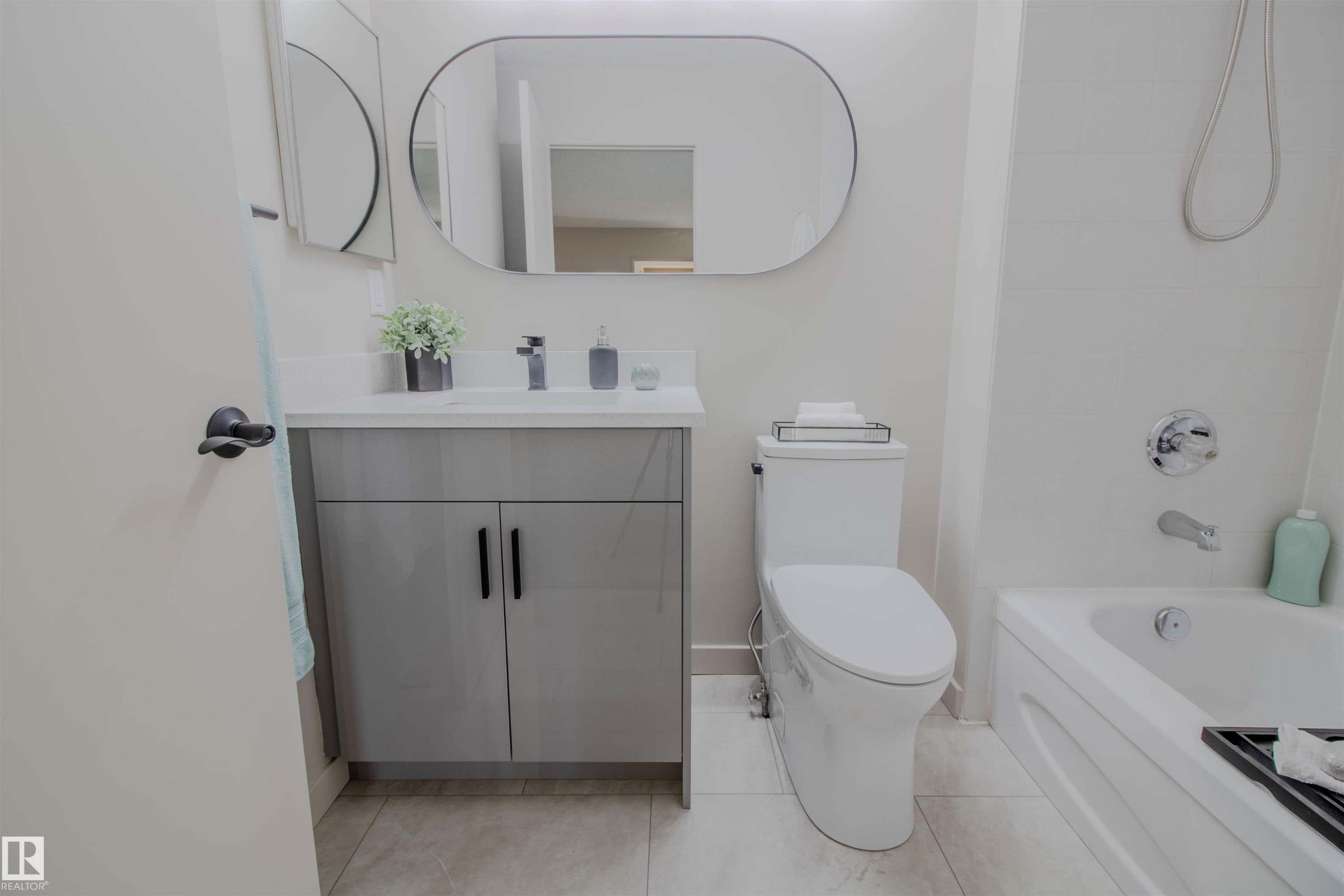 Contemporary bathroom featuring a white bathtub, a modern toilet, and a vanity with a light gray cabinet, white countertop, and a rectangular undermount sink - 5935 189 Street, Edmonton, AB - Indoor Photo Showing Bathroom