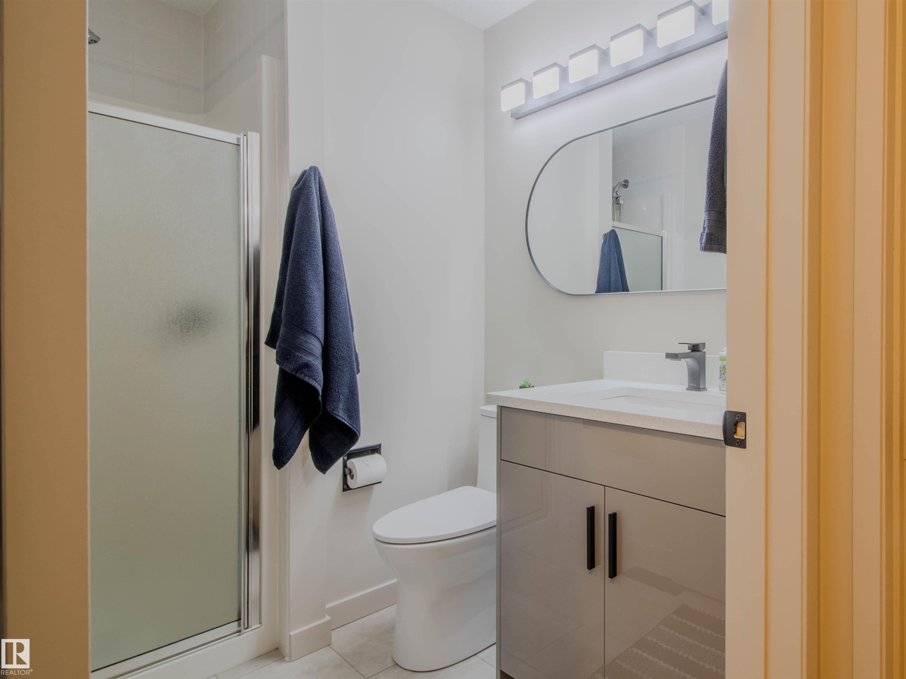 Bathroom featuring a glass-enclosed shower, a modern vanity with a white countertop, an oval wall-mounted mirror, and a sleek light fixture - 5935 189 Street, Edmonton, AB - Indoor Photo Showing Bathroom