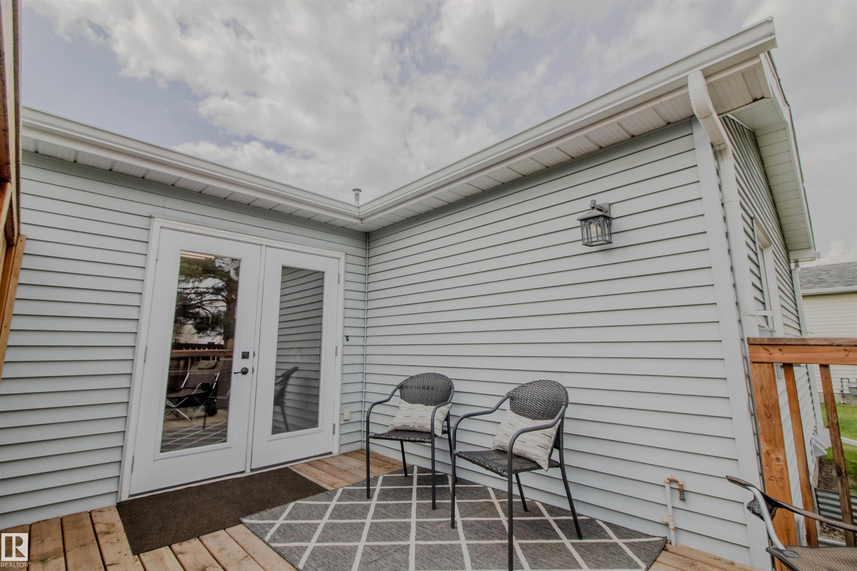 Deck area featuring light blue siding, white French doors, an exterior wall lantern, and wood-finish decking - 5935 189 Street, Edmonton, AB - Outdoor With Exterior