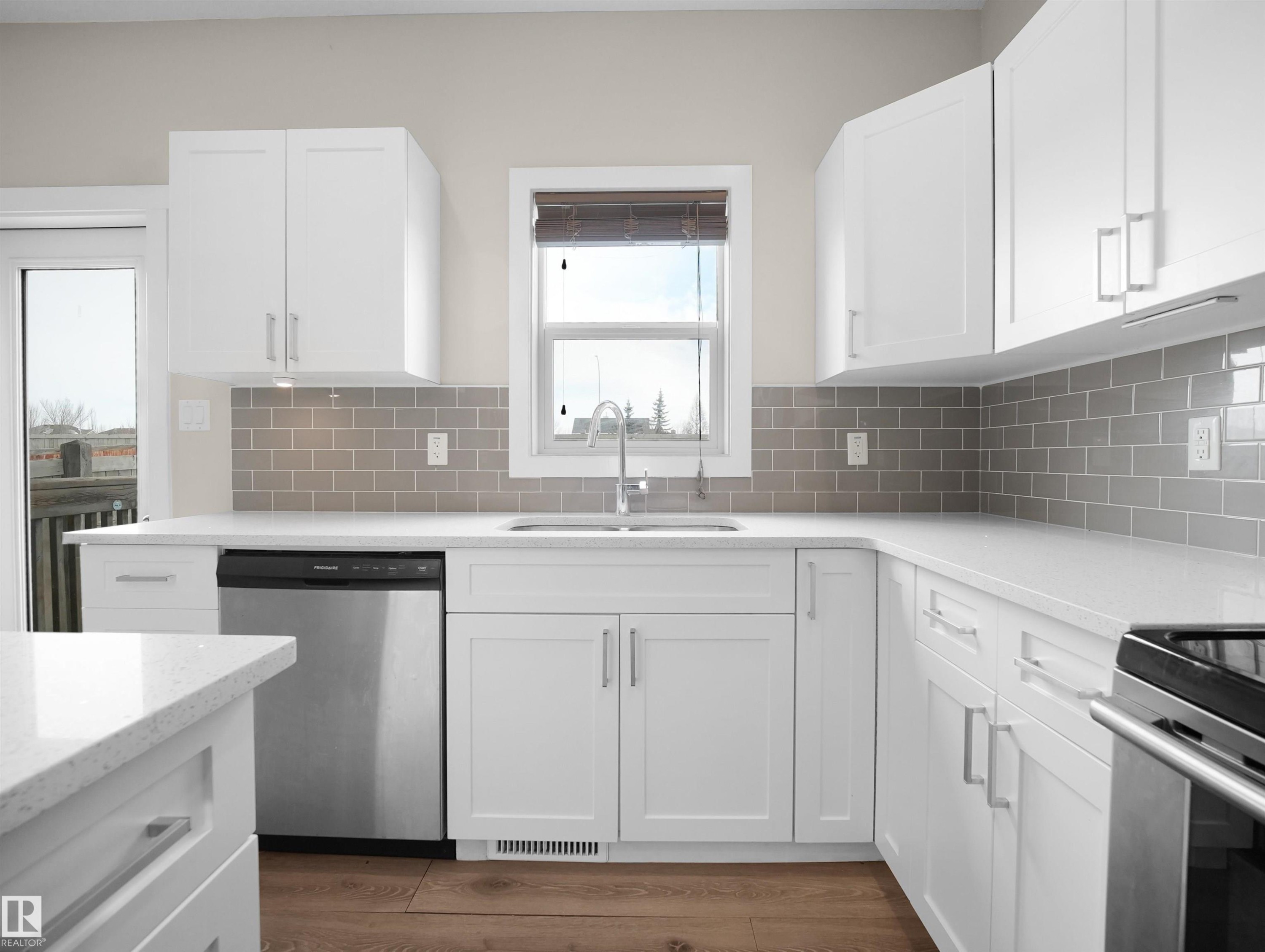 Modern kitchen featuring white shaker cabinetry, light-toned countertops, a gray subway tile backsplash, stainless steel appliances, and wood-finish flooring - 8921 217 Street Nw, Edmonton, AB - Indoor Photo Showing Kitchen With Upgraded Kitchen