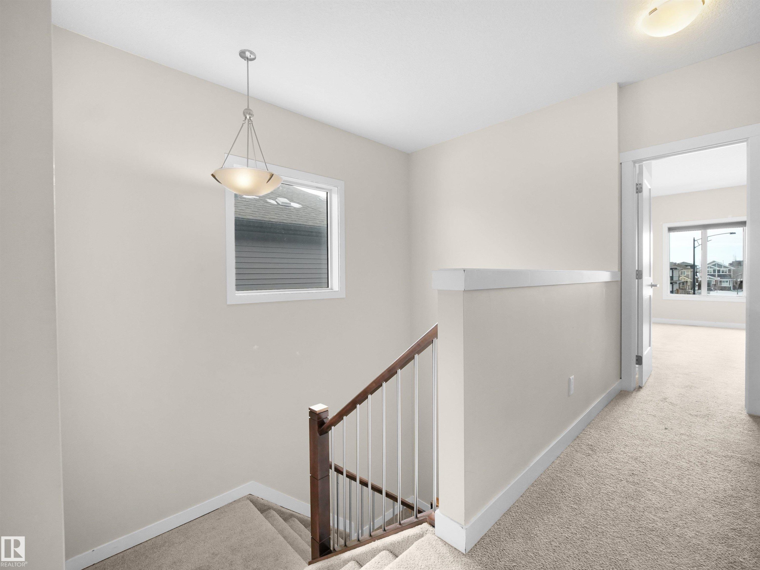 Upper-level landing featuring neutral carpeting, a staircase with dark wood handrail and white spindles, and a pendant light fixture - 8921 217 Street Nw, Edmonton, AB - Indoor Photo Showing Other Room