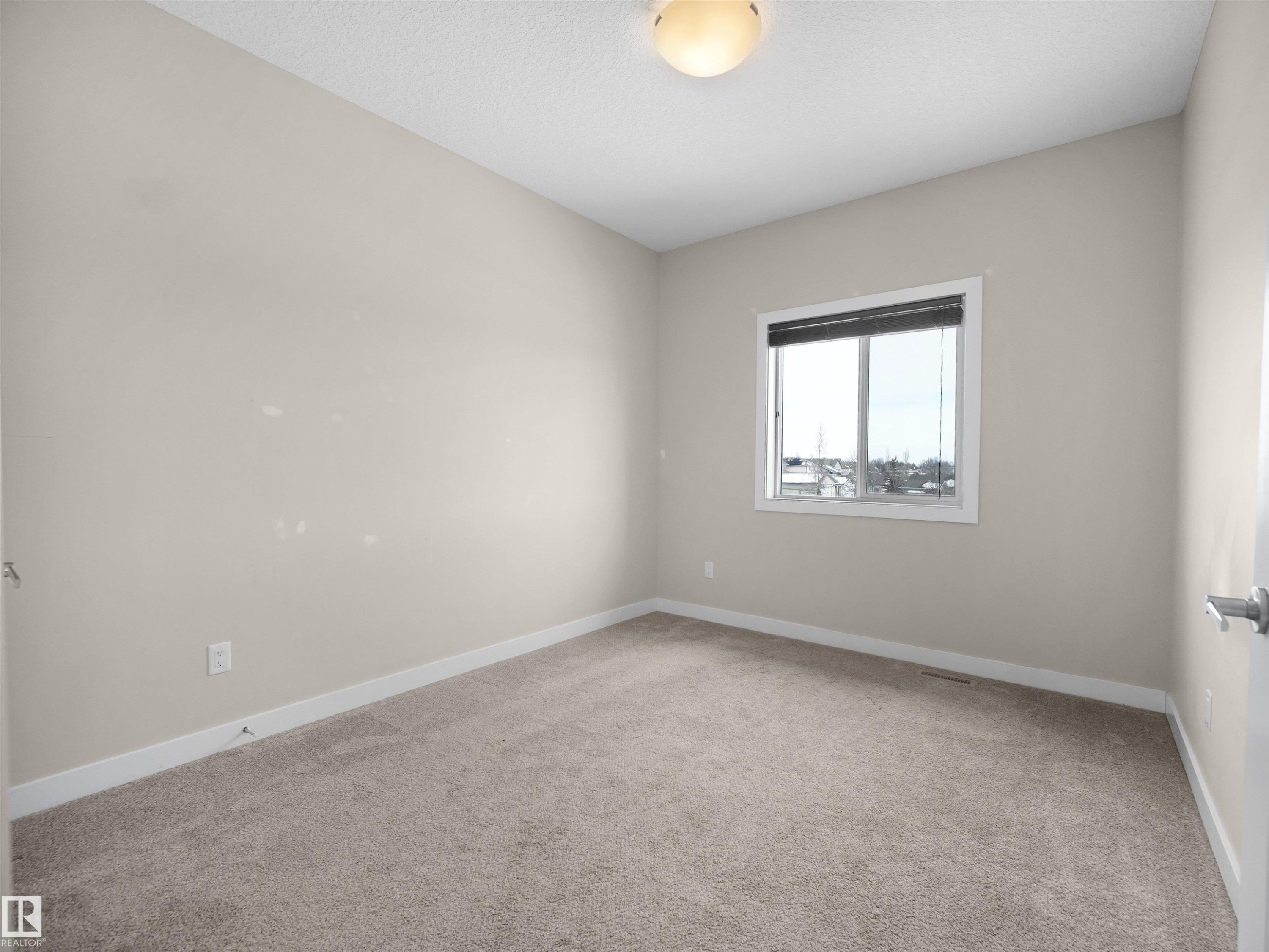 Neutral beige carpeting, light beige wall paint, white trim, and a window featuring horizontal blinds - 8921 217 Street Nw, Edmonton, AB - Indoor Photo Showing Other Room