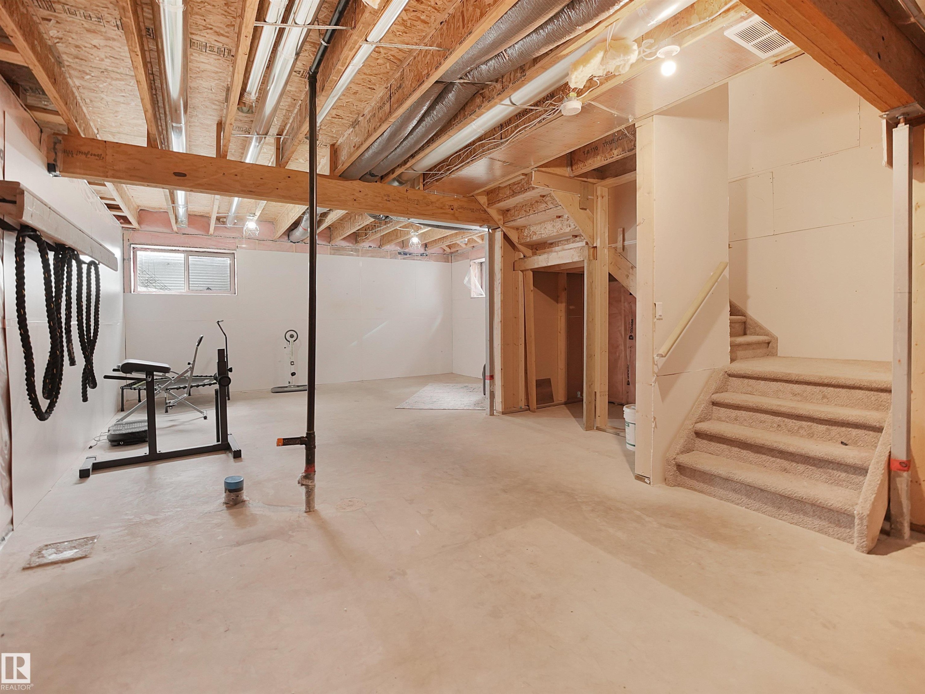 Unfinished basement featuring exposed wood joists, concrete flooring, egress window, and carpeted stairs with wood railing - 8921 217 Street Nw, Edmonton, AB - Indoor Photo Showing Basement