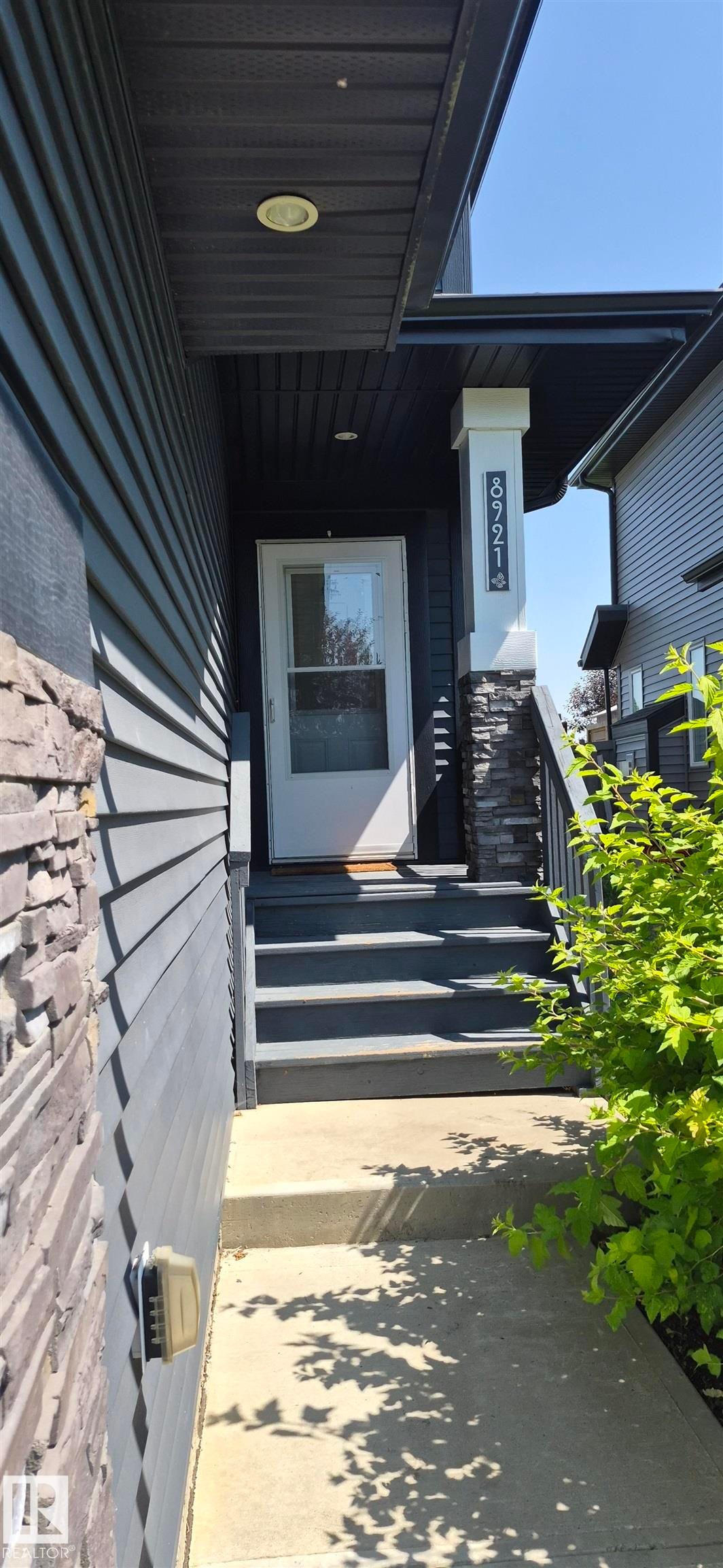 Entryway featuring a white storm door, dark exterior siding, and stone veneer accents - 8921 217 Street Nw, Edmonton, AB - Outdoor