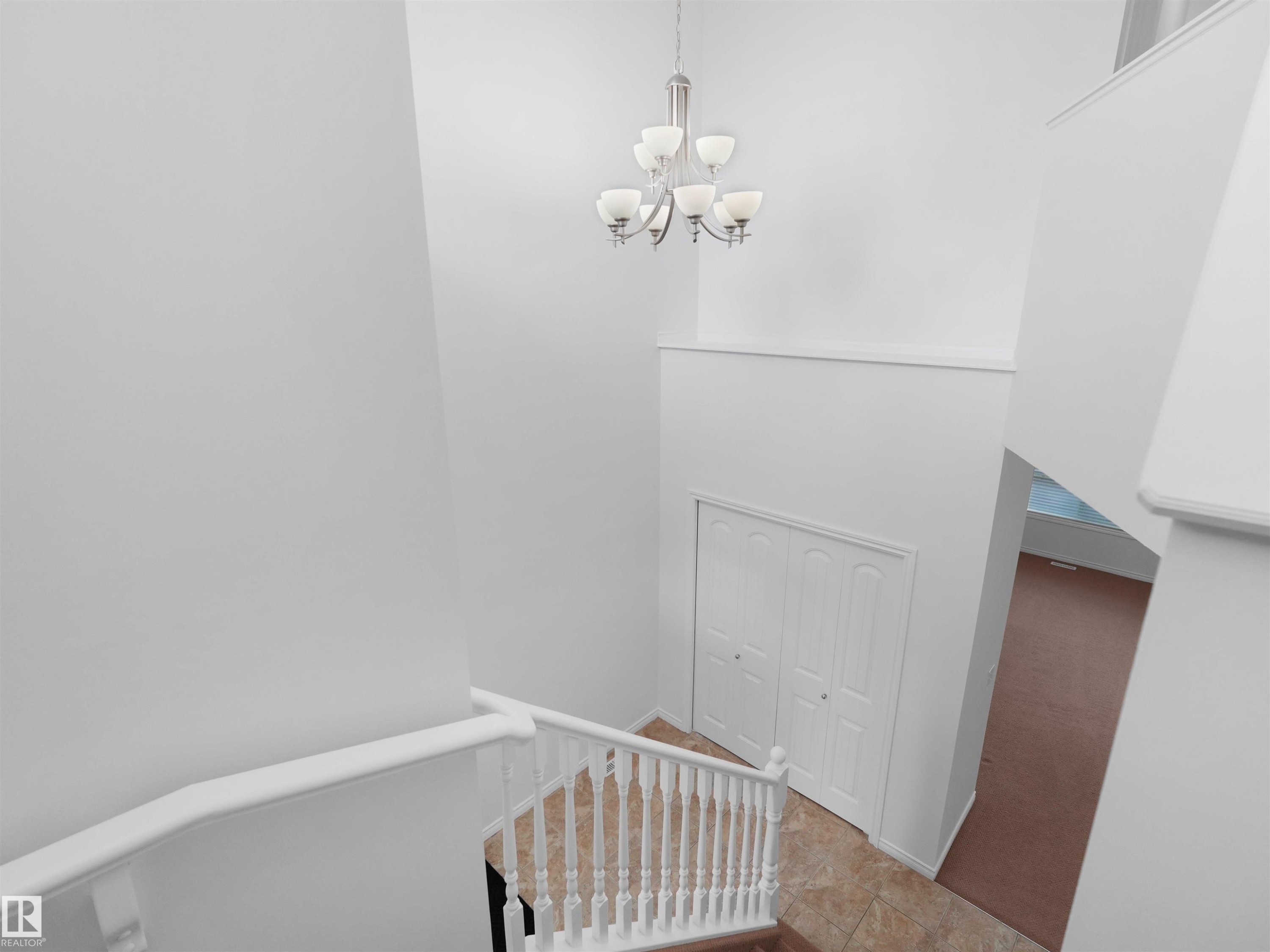 Foyer featuring a contemporary chandelier, white railings, tile flooring, and a bifold closet door - 2017 32A Street, Edmonton, AB - Indoor Photo Showing Other Room