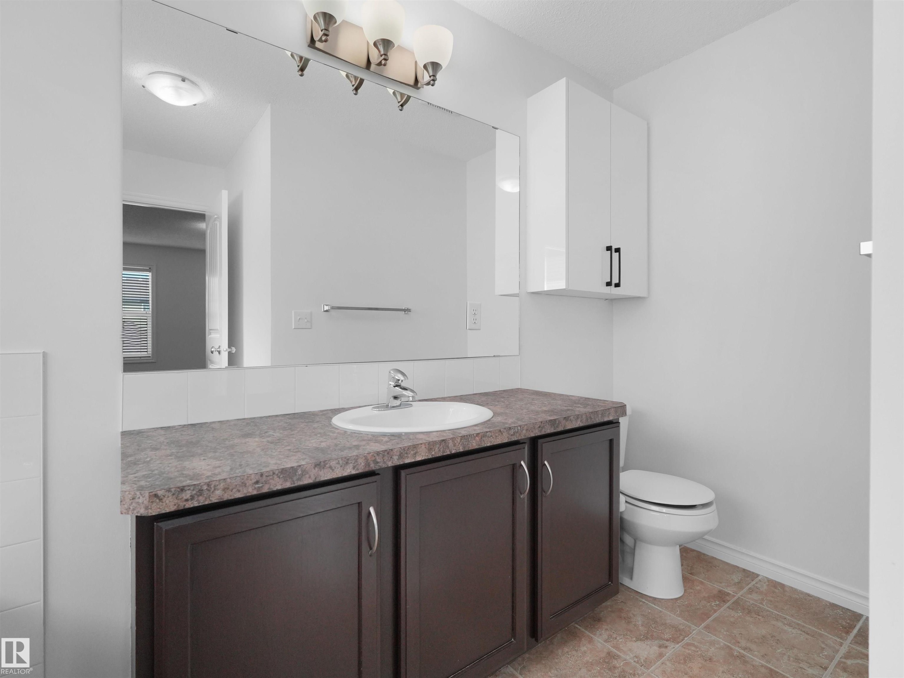 Bathroom featuring a vanity with a dark wood-finish base and a mottled countertop, an integrated sink, and a wall-mounted mirror - 2017 32A Street, Edmonton, AB - Indoor Photo Showing Bathroom