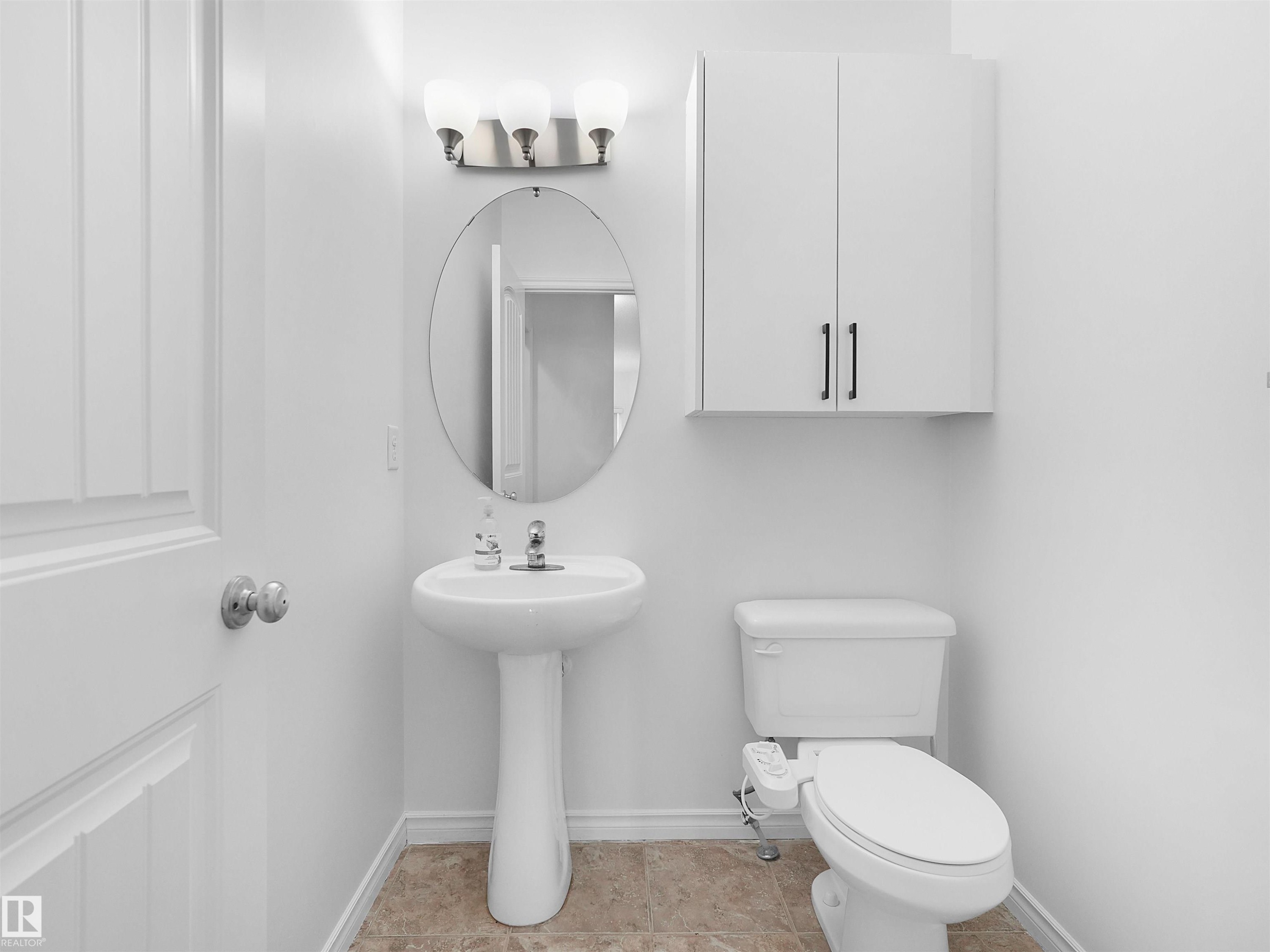 Pedestal sink with an oval mirror, modern vanity lighting, white wall-mounted cabinetry, and light-toned floor tiling - 2017 32A Street, Edmonton, AB - Indoor Photo Showing Bathroom