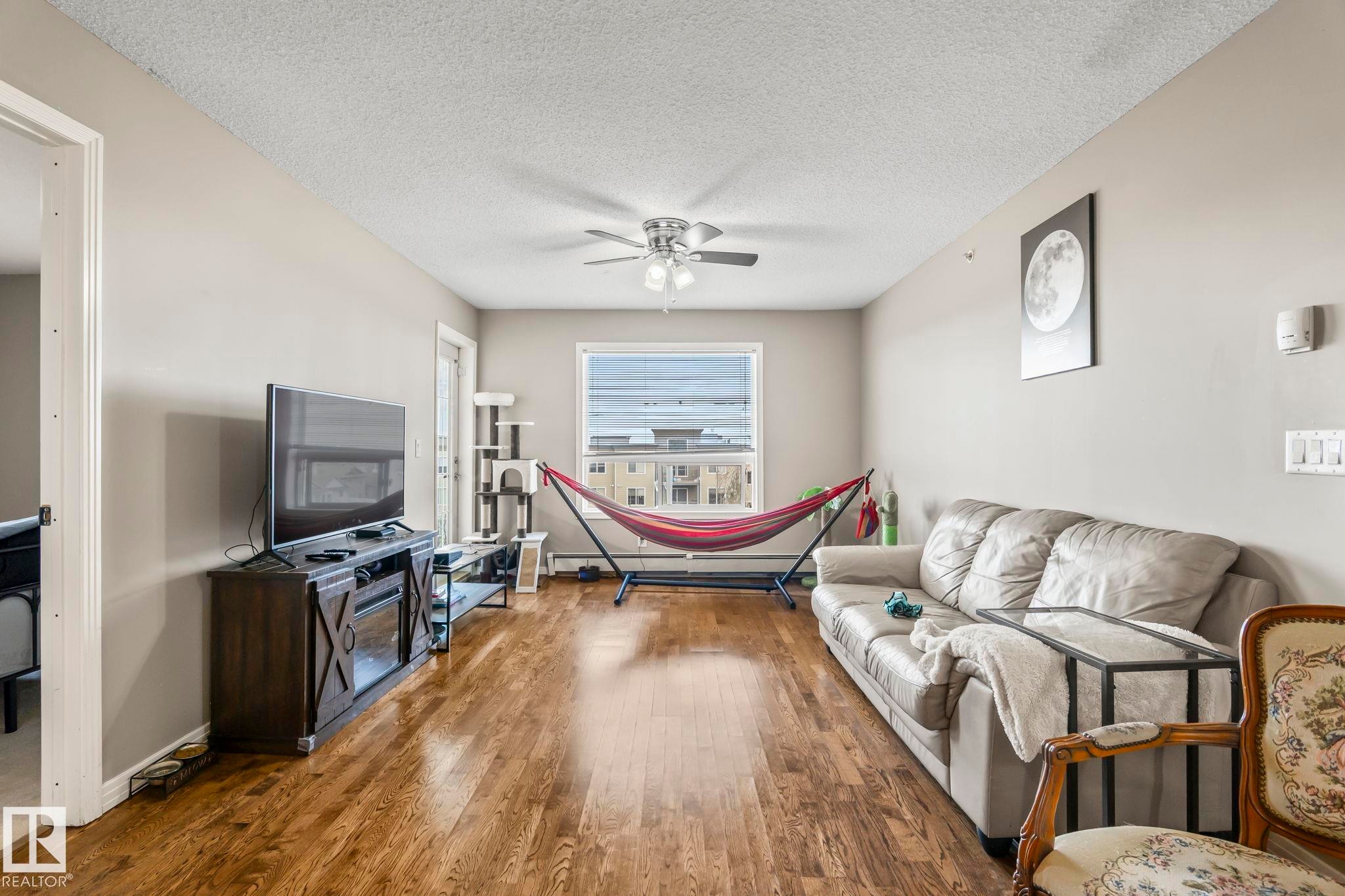 Spacious living area featuring wood-finish flooring, light neutral wall tones, and a ceiling fan - 412 5005 165 Avenue Nw, Edmonton, AB - Indoor Photo Showing Living Room