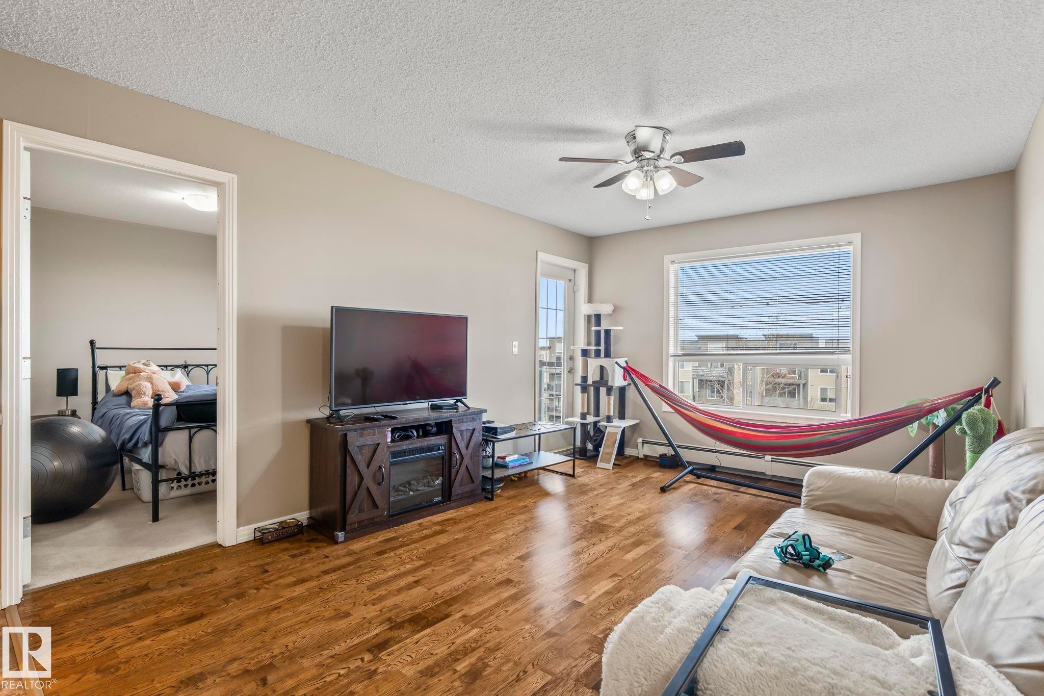 Spacious living area featuring wood-finish flooring, a ceiling fan with integrated lighting, and neutral wall tones - 412 5005 165 Avenue Nw, Edmonton, AB - Indoor Photo Showing Living Room