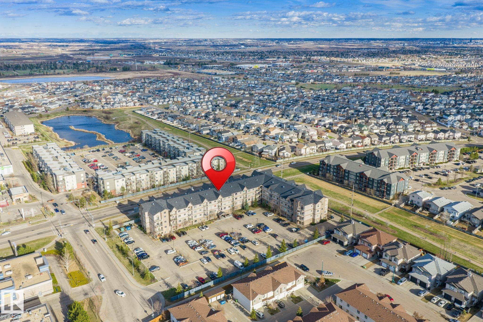 Multi-story residential building featuring a gabled roofline, multiple balconies, and an expansive parking area - 412 5005 165 Avenue Nw, Edmonton, AB - Outdoor With View