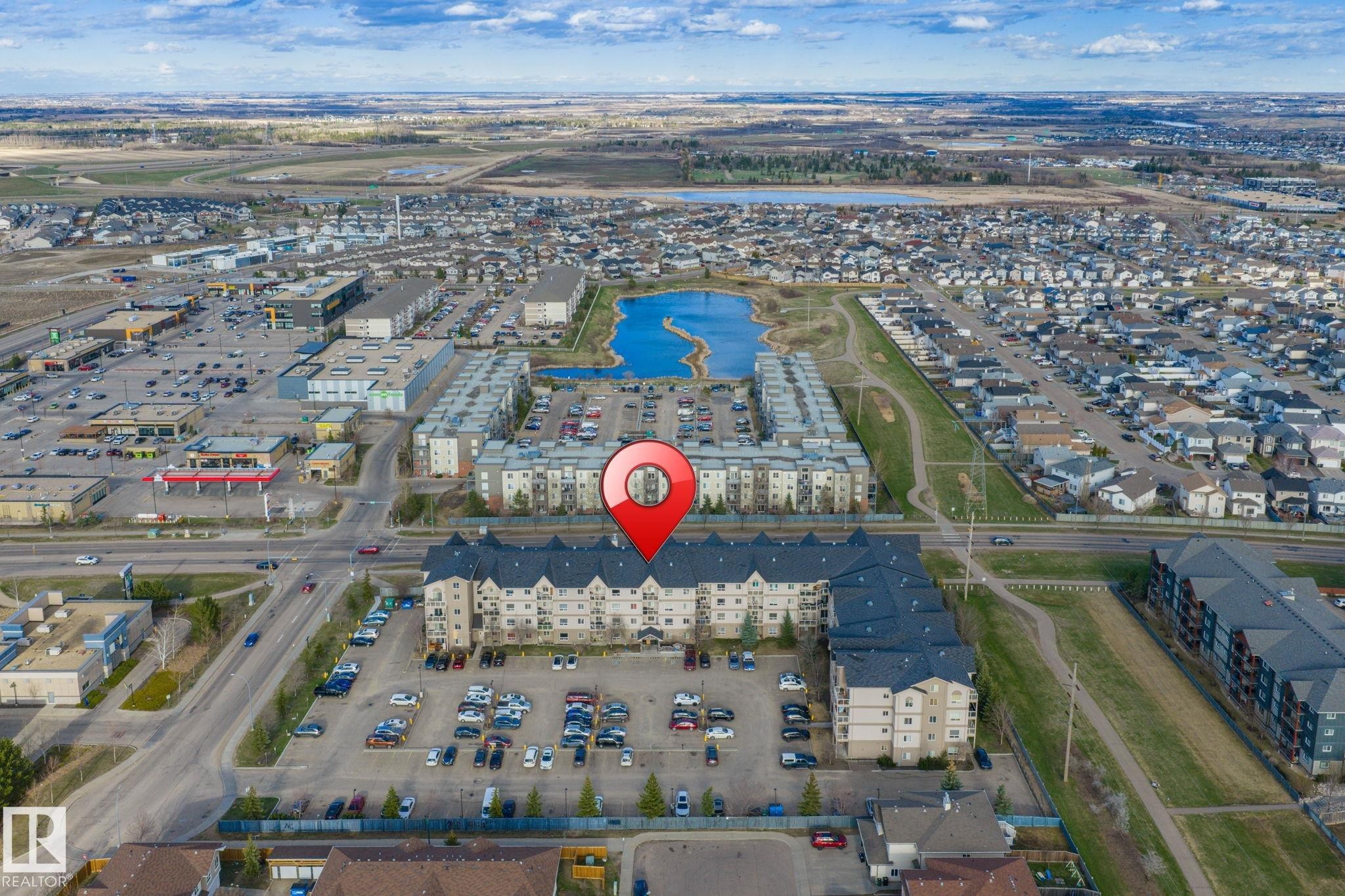 Multi-story building featuring light-colored siding and dark roofing, surrounded by a paved parking area - 412 5005 165 Avenue Nw, Edmonton, AB - Outdoor With View