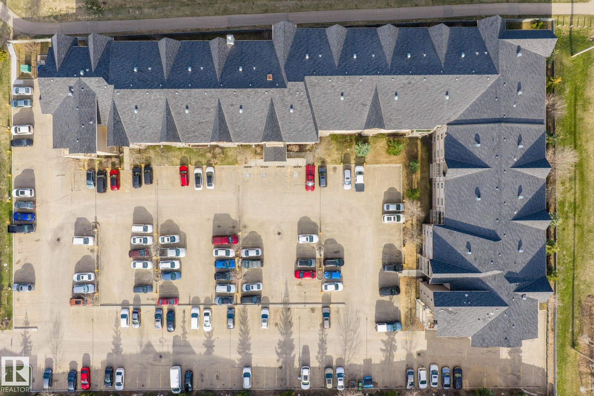 Large asphalt parking lot with multiple parking spaces and a multi-story building featuring a dark gray shingle roof - 412 5005 165 Avenue Nw, Edmonton, AB - With View
