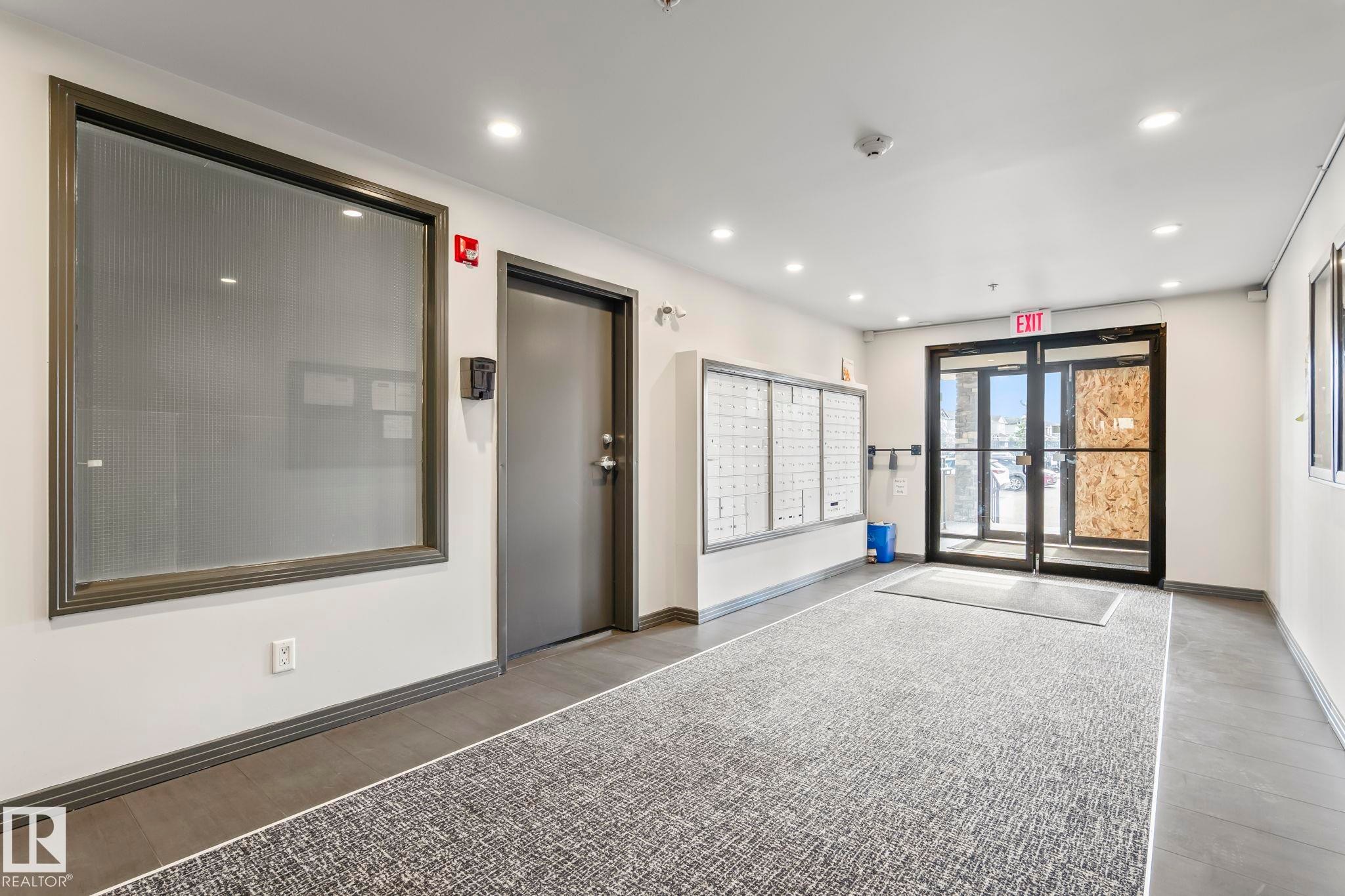 Building entrance featuring commercial-style glass doors, wall-mounted mailboxes, recessed lighting, and a textured area rug - 412 5005 165 Avenue Nw, Edmonton, AB - Indoor Photo Showing Other Room