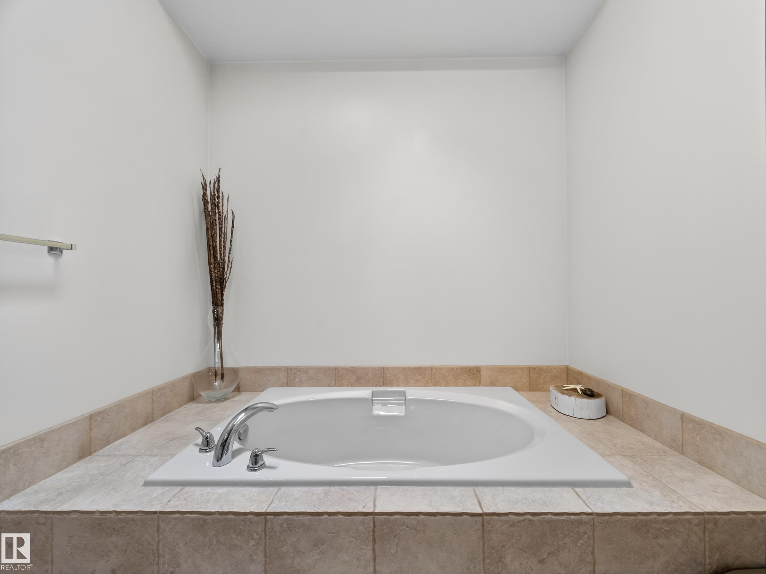 White drop-in tub with chrome fixtures, set within a tiled surround featuring neutral-toned ceramic tiles - 569 Butterworth Way, Edmonton, AB - Indoor Photo Showing Bathroom